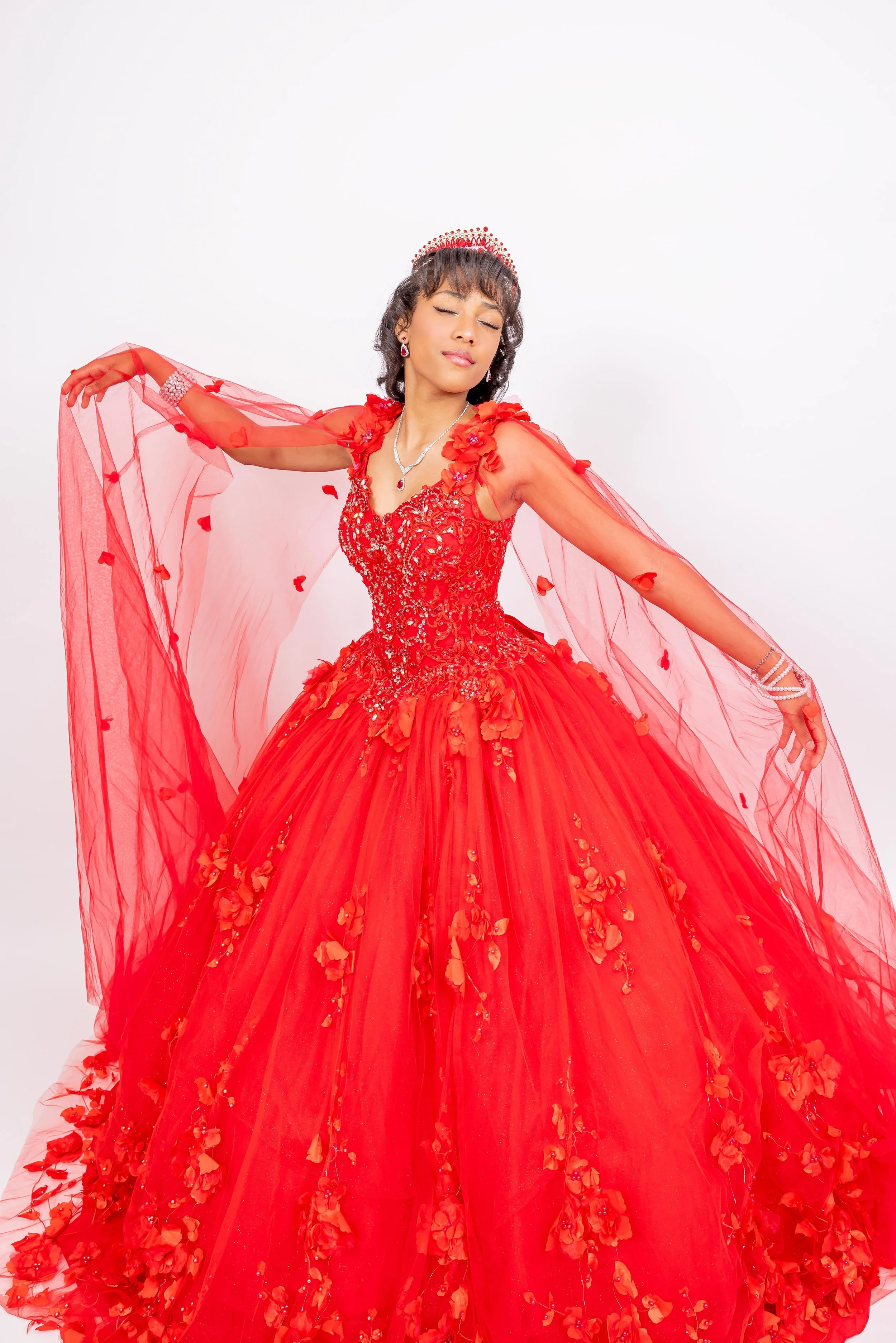 Mujer con vestido de noche rojo con detalles de flores, puesta con expresión de tranquilidad y ojos cerrados, en fondo blanco.