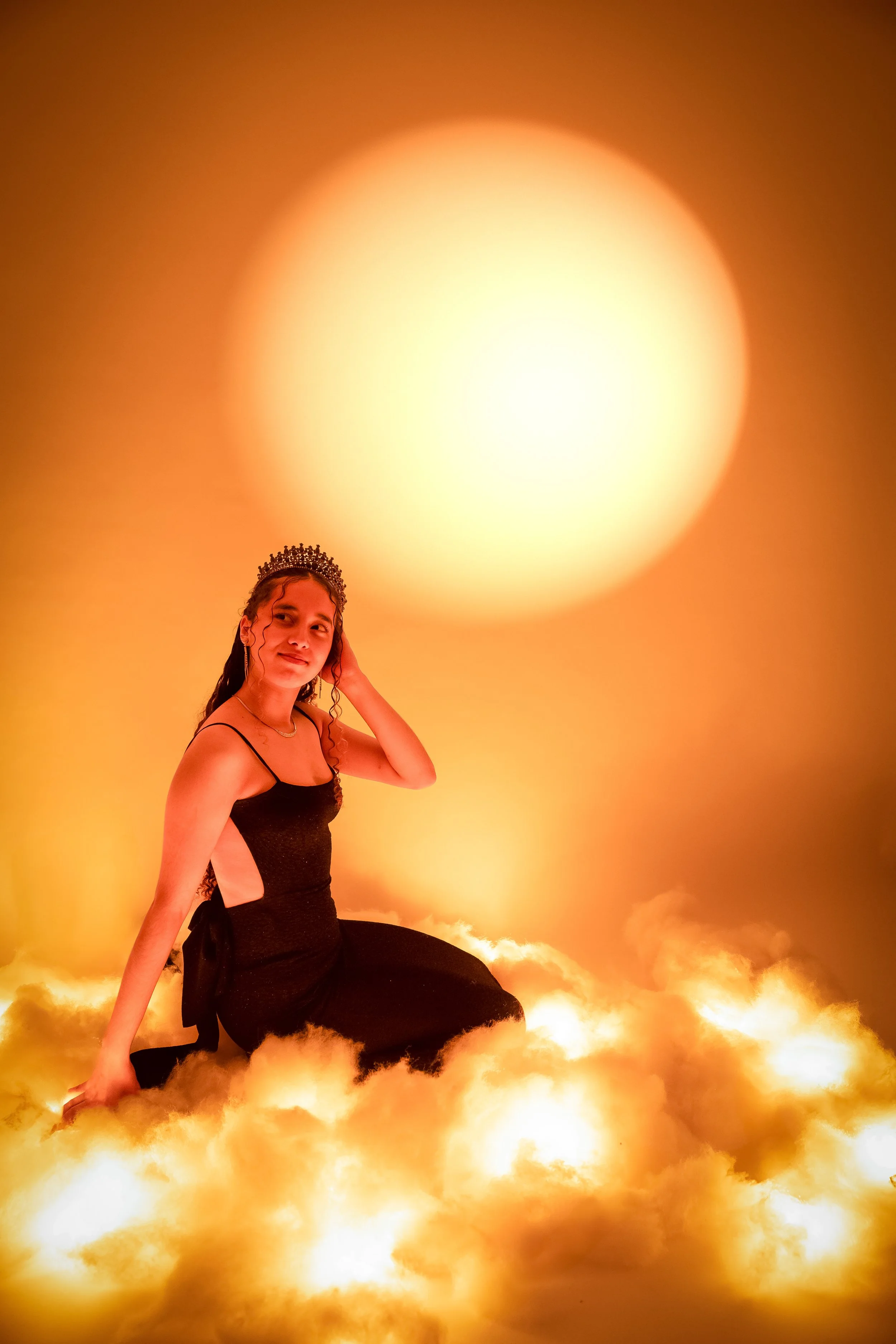 Joven con tiara en una escenografía de nubes y un sol gigante en el fondo.