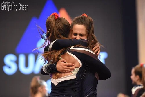 Two cheerleaders hugging on stage during a cheerleading competition.