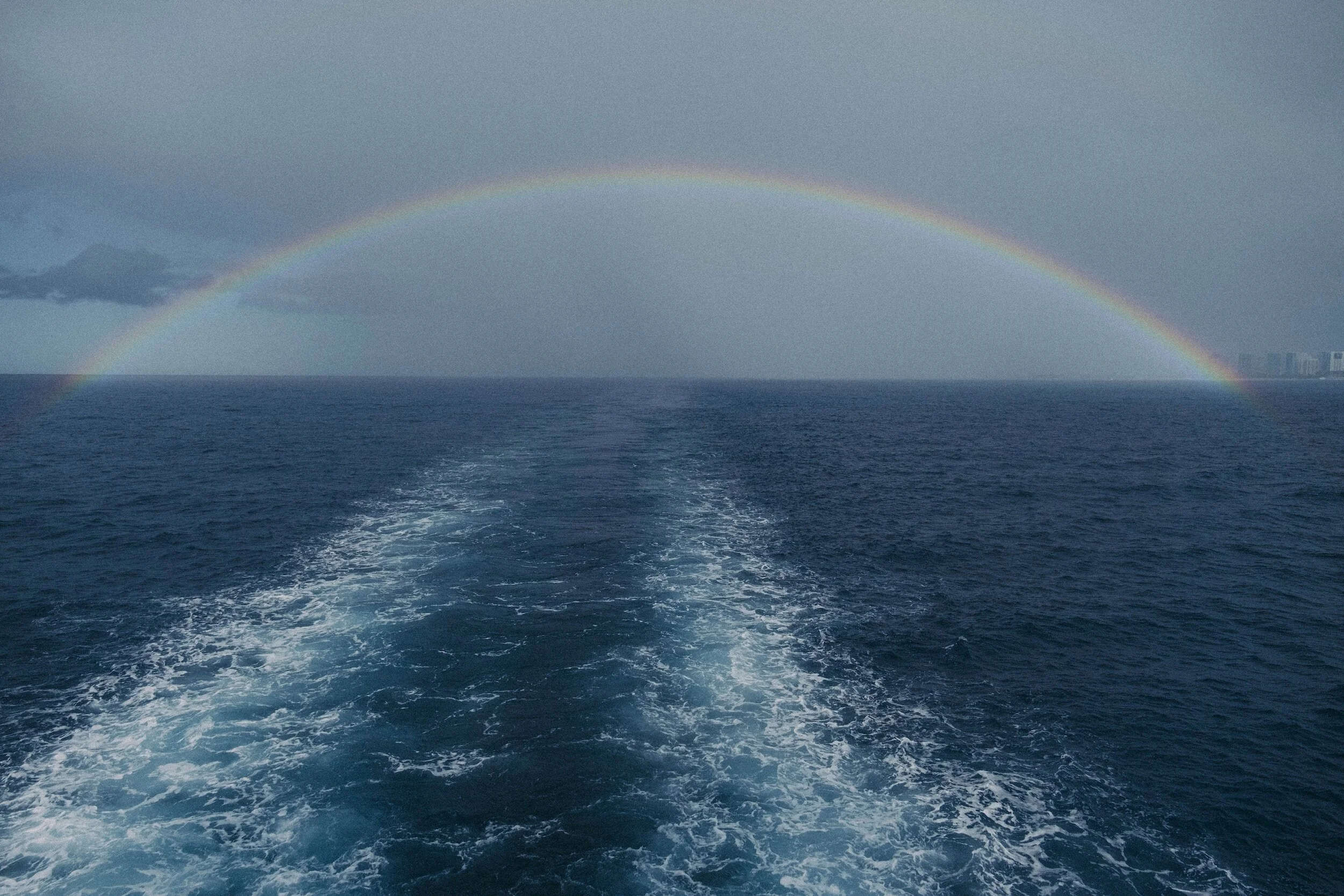 Rainbow over horizon and ship's wake in the center