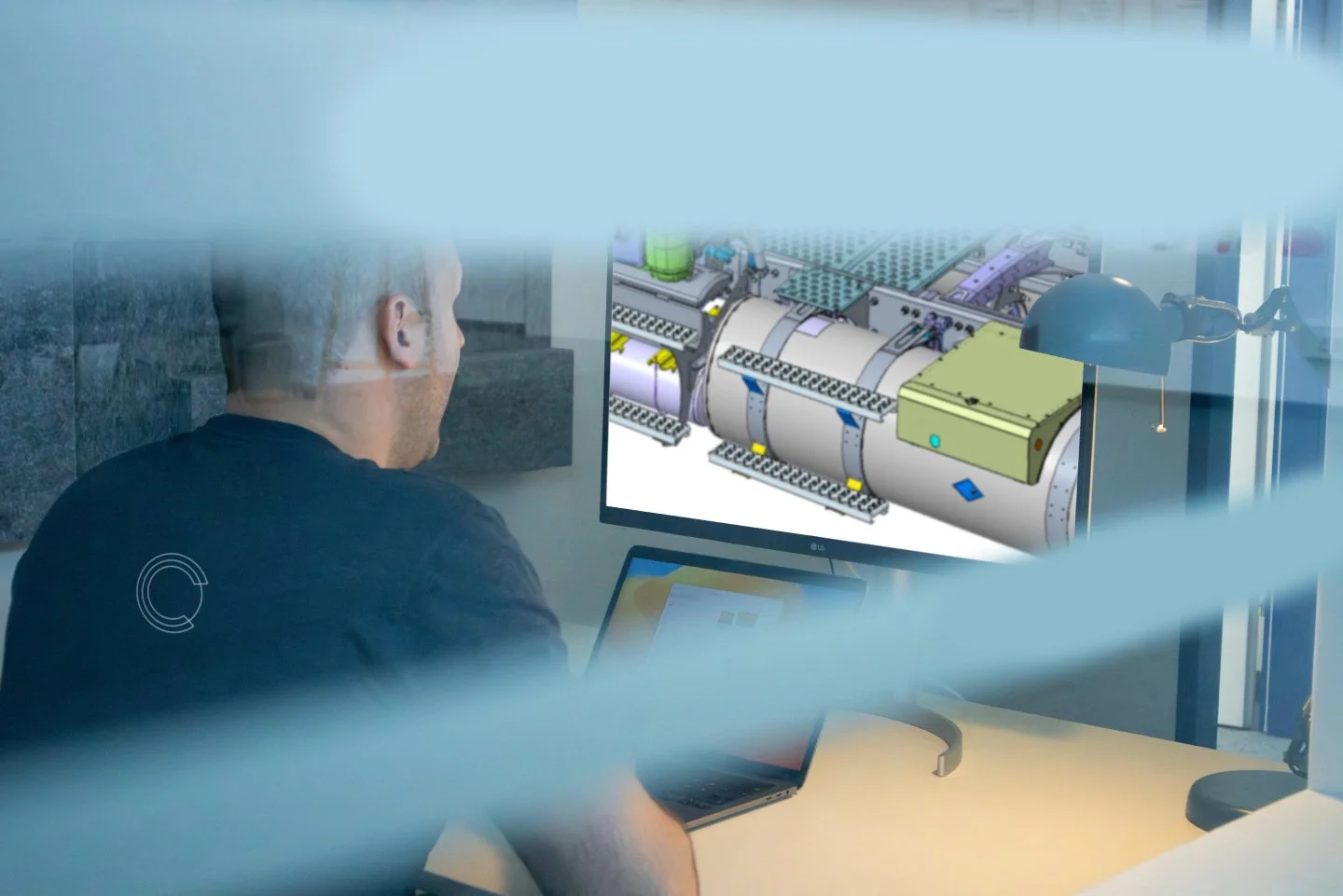 Ein Mann sitzt vor einem Computerbildschirm mit einer technischen Illustration einer Maschine, die aus mehreren Komponenten besteht.