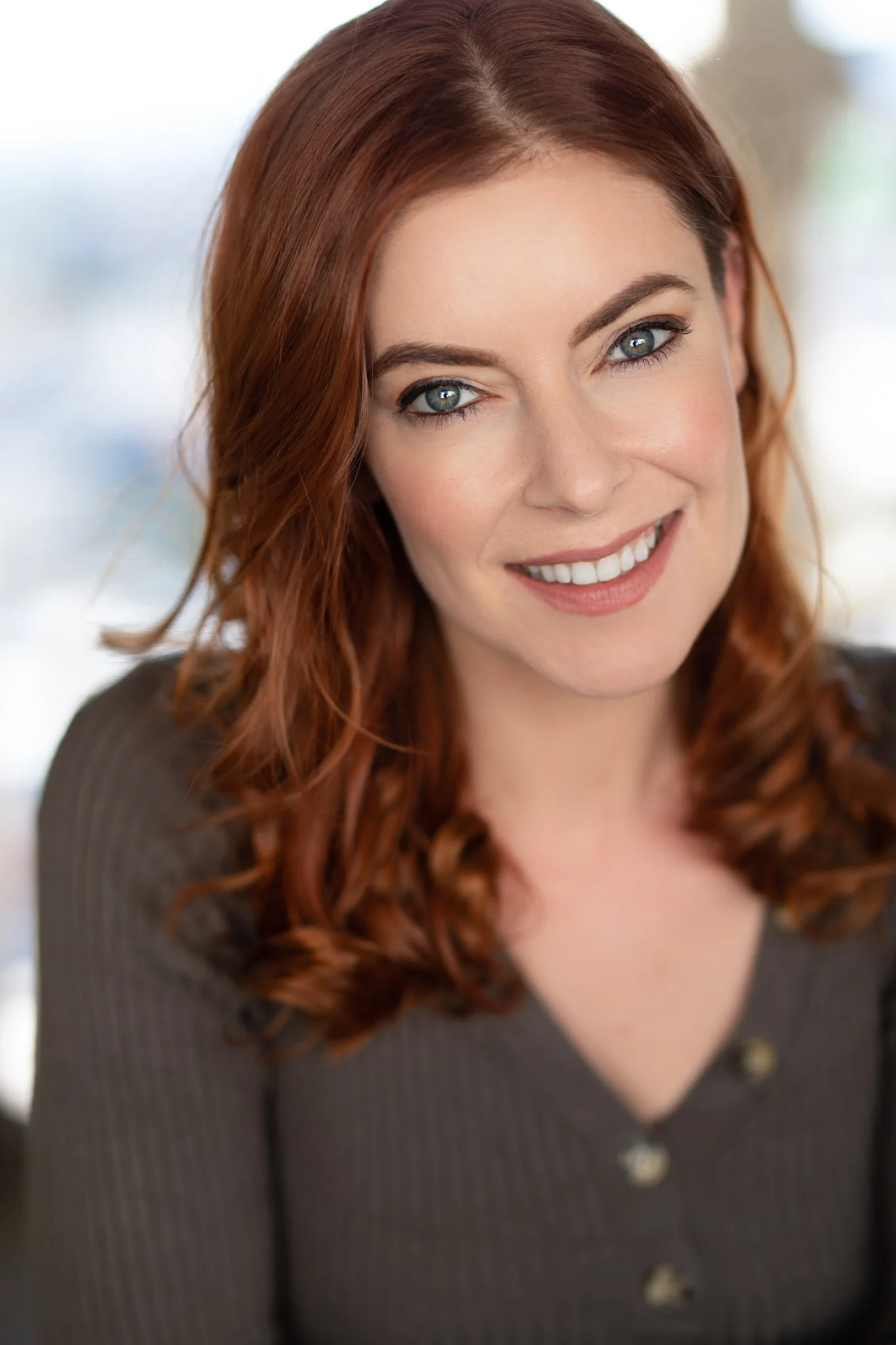 Close-up of a woman with red hair and blue eyes smiling at the camera.