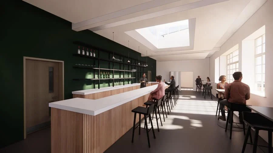 Modern bar with a long counter, stools, people sitting, large windows, and natural light streaming in from a skylight.