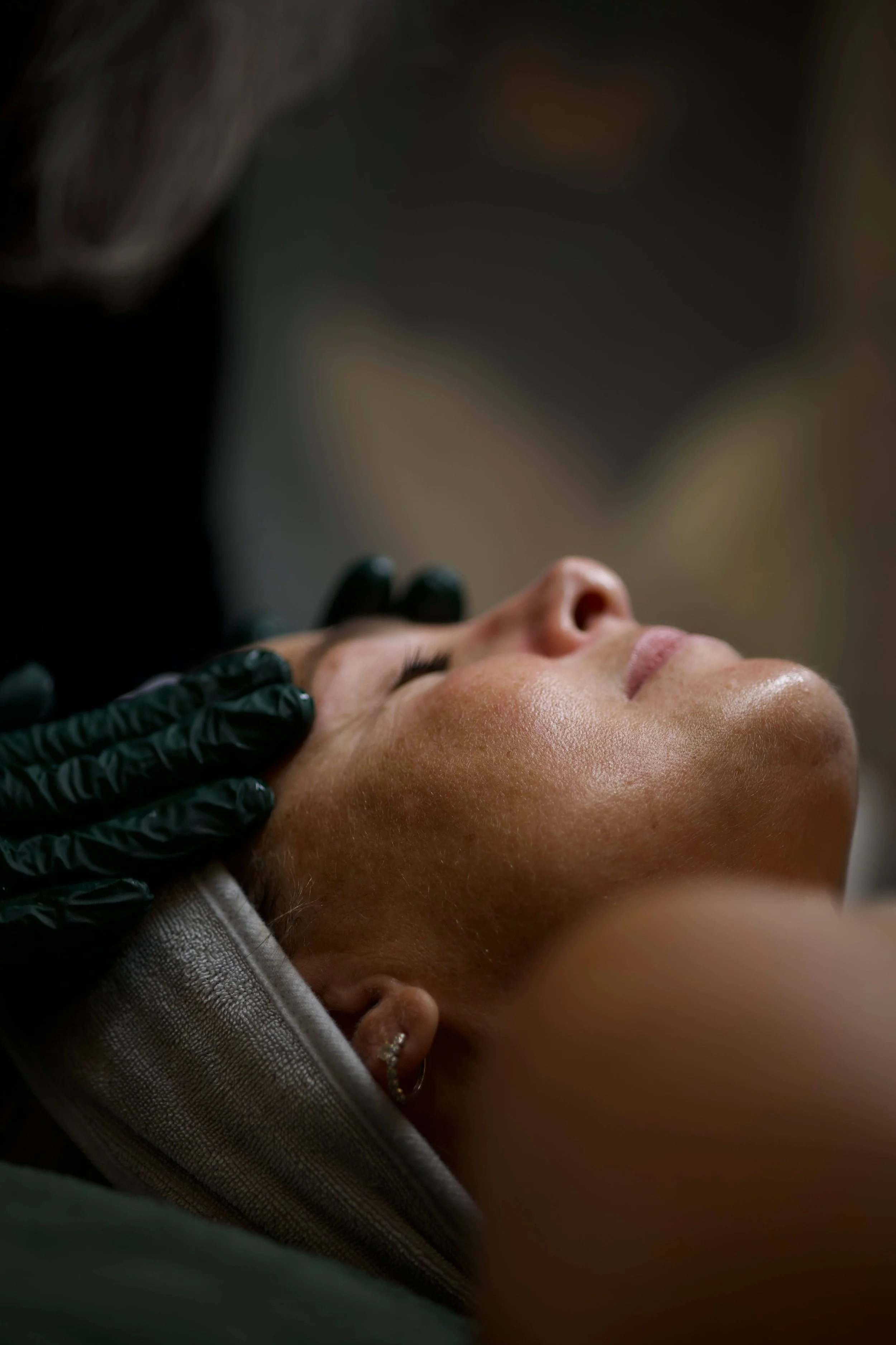lient receiving a relaxing facial treatment at Bombshell Aesthetics in Bedford, NH, with a provider wearing black gloves gently massaging the forehead in a softly lit treatment room.