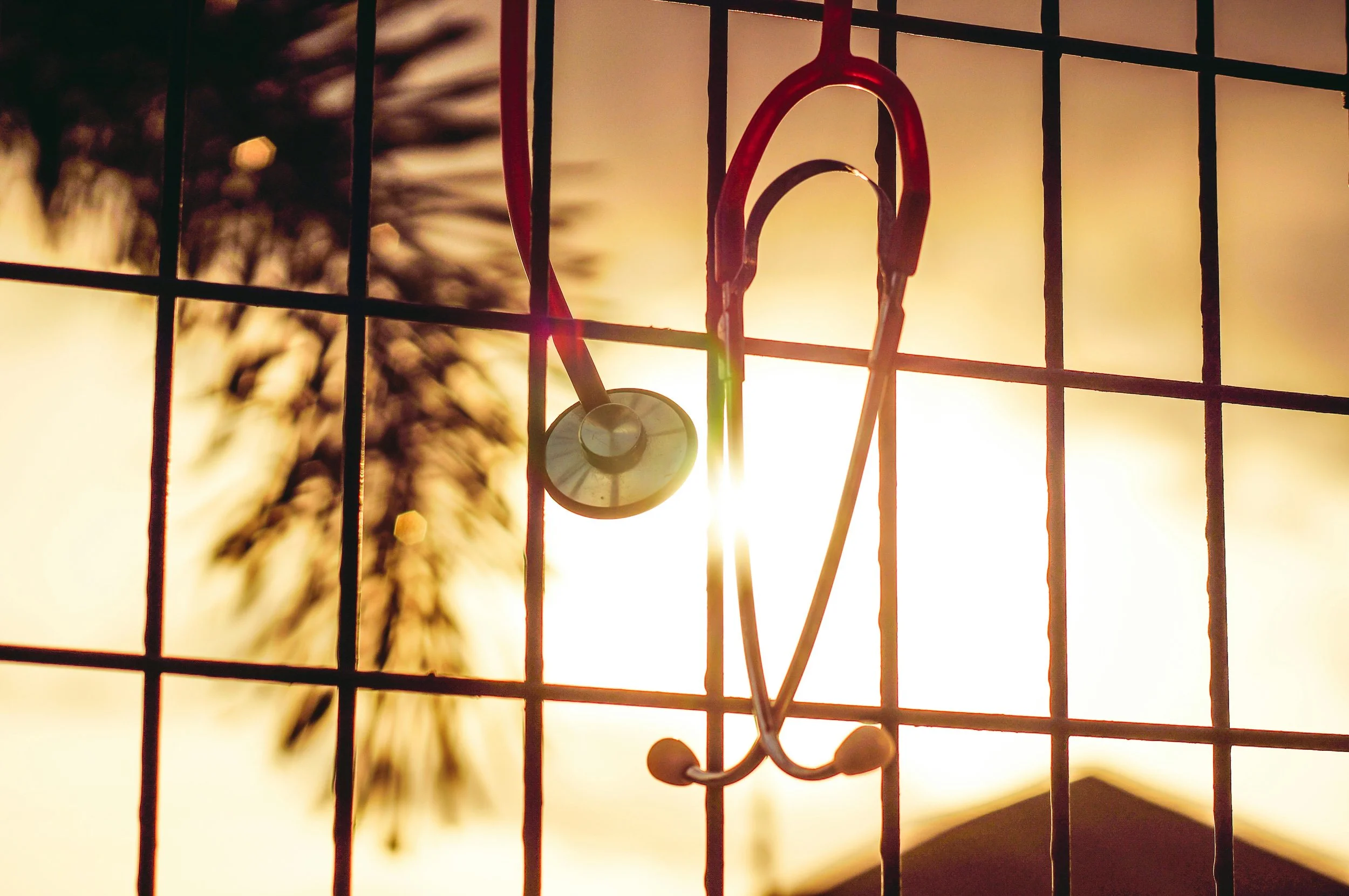 A stethoscope hanging on a wire fence during sunset, with blurred trees in the background.