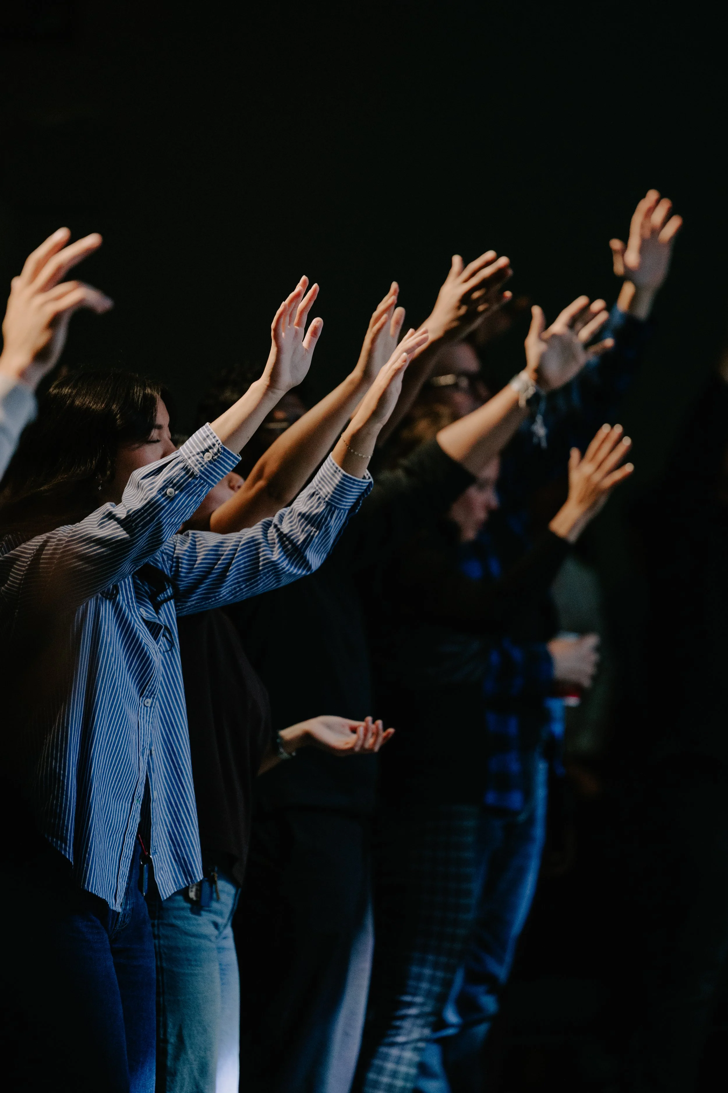 Group of people standing with raised hands in a dark setting, possibly at a concert or event.
