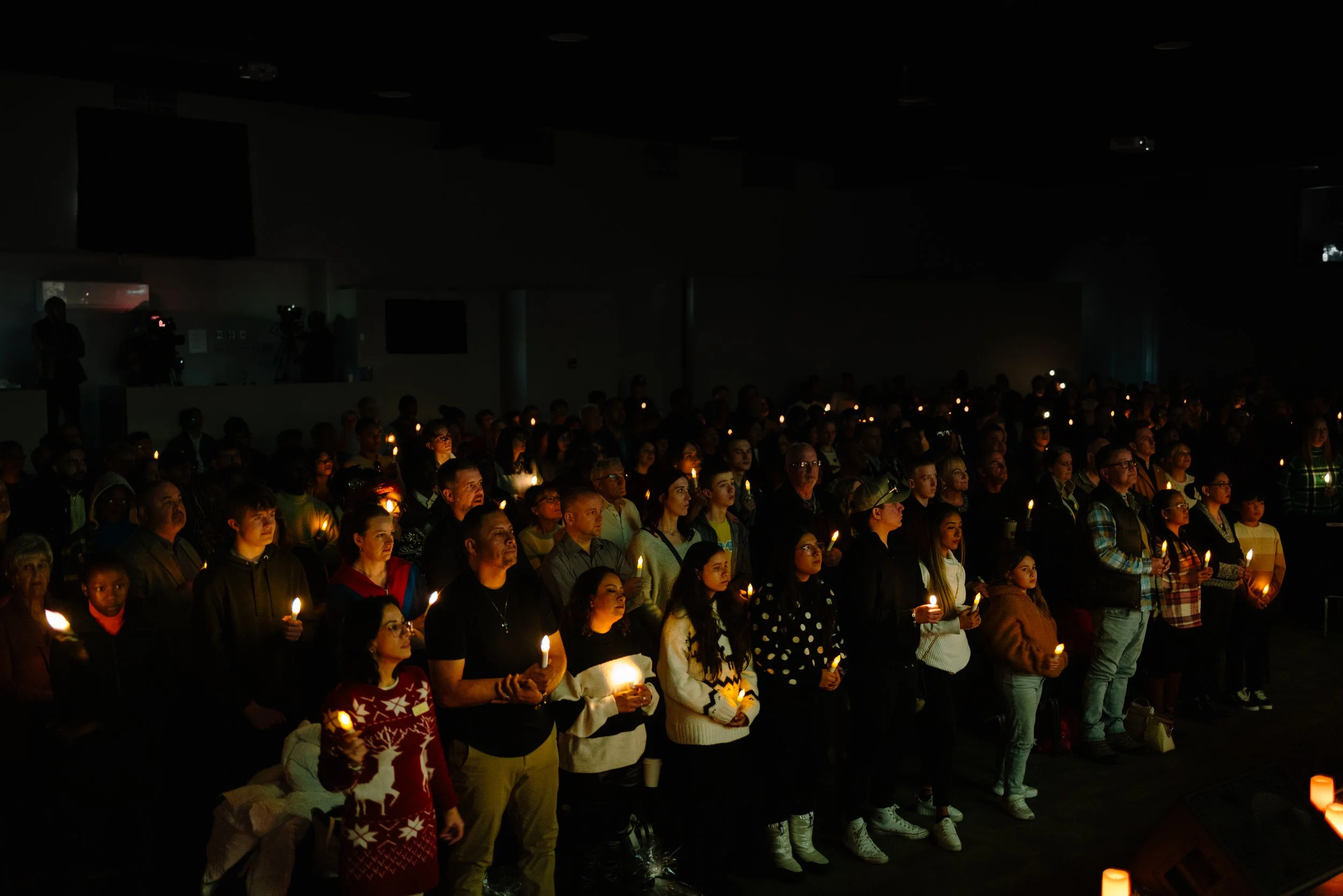 A large group of people standing in a dark room, holding lit candles during Christmas Eve.