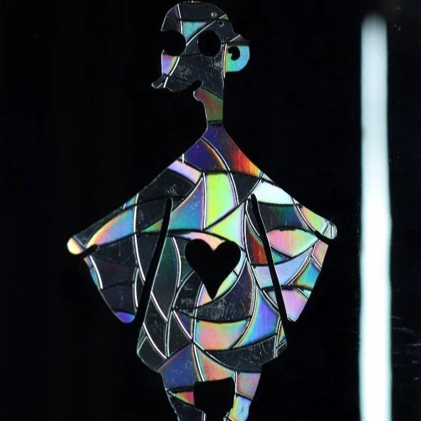 Decorative mirror in the shape of a woman with a heart cutout in the chest and a small heart on the skirt, reflecting colorful light.