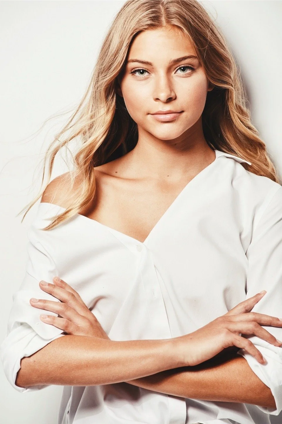 Person with folded arms wearing a white shirt, blonde hair, neutral expression.
