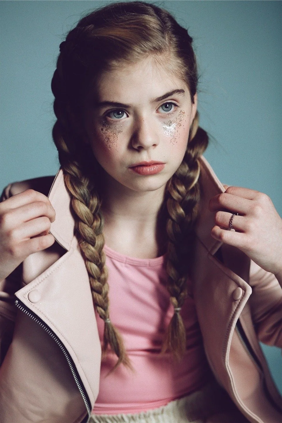 Young girl with braided hair wearing pink jacket and glitter makeup