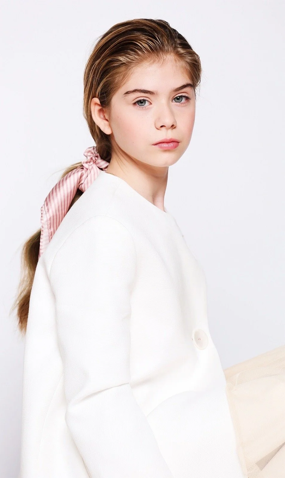 Young person with long hair tied with a pink bow wearing a white outfit.