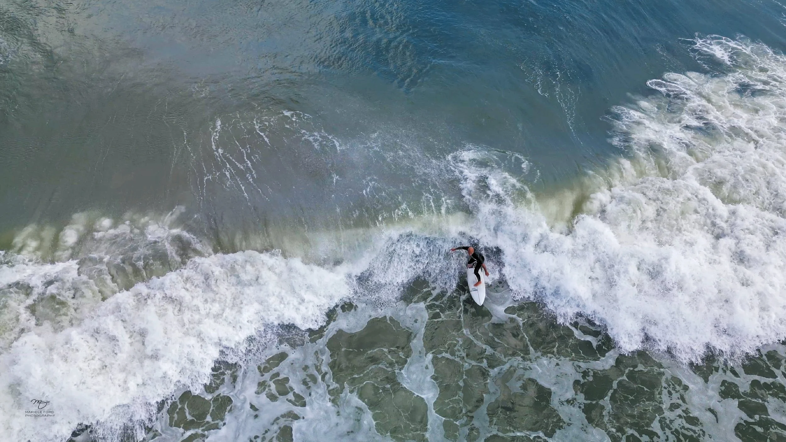 A surfer riding a wave in the ocean, captured from a high angle.