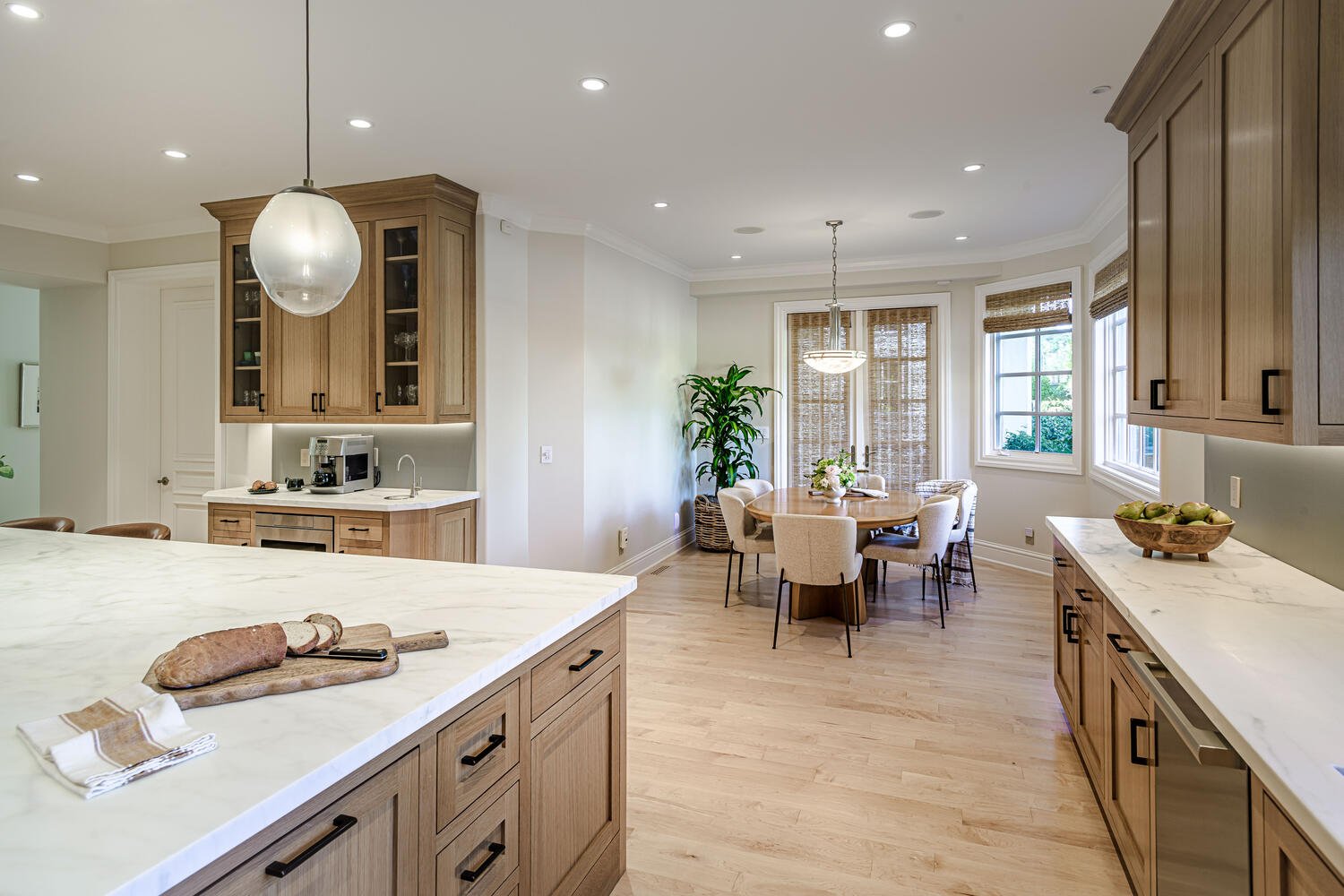 Bright kitchen with wooden cabinets and a round dining table near windows, decorated with a plant and a flower arrangement.
