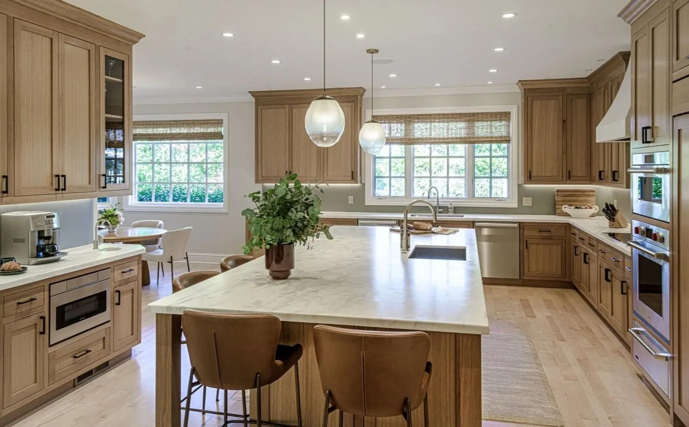 Bright kitchen with wooden cabinets, a large island with a marble countertop, pendant lights, and windows with blinds.