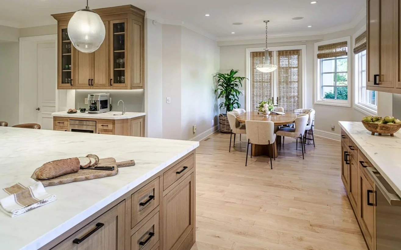 Bright kitchen with wooden cabinets and a round dining table near windows, decorated with a plant and a flower arrangement.