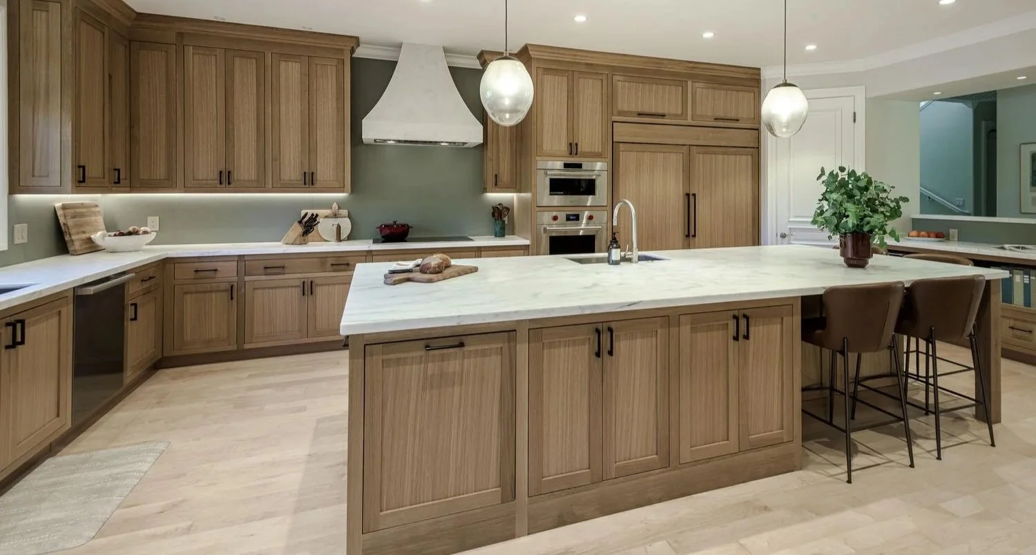 Modern kitchen with wooden cabinets, marble island, and pendant lighting, featuring appliances and a potted plant.