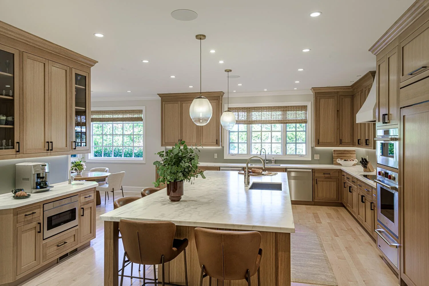 Bright kitchen with wooden cabinets, a large island with a marble countertop, pendant lights, and windows with blinds.