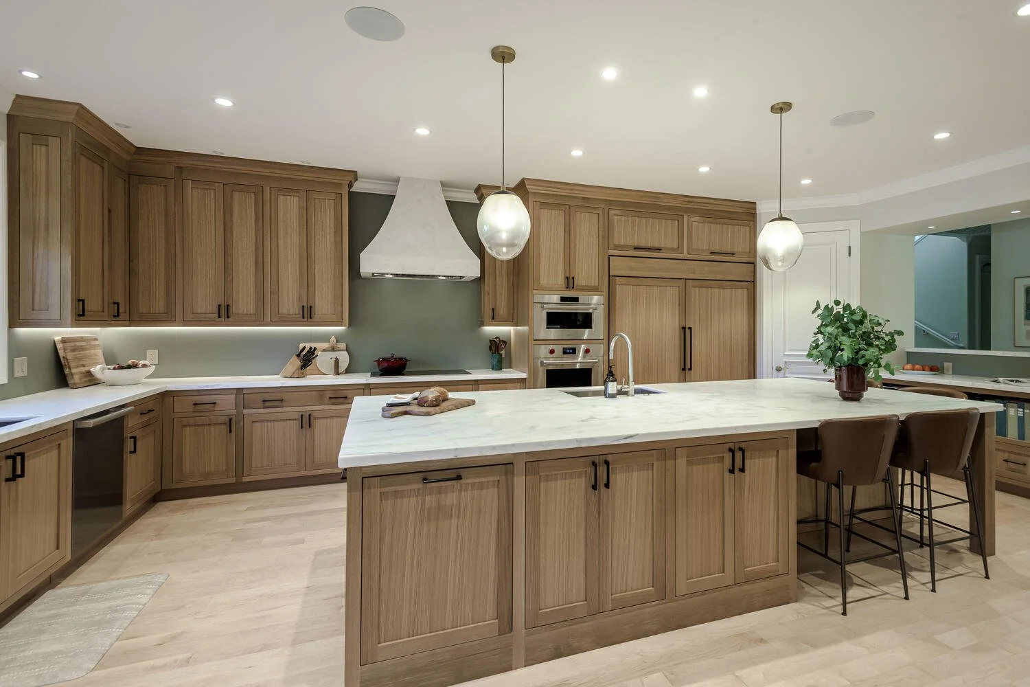 Modern kitchen with wooden cabinets, marble island, and pendant lighting, featuring appliances and a potted plant.