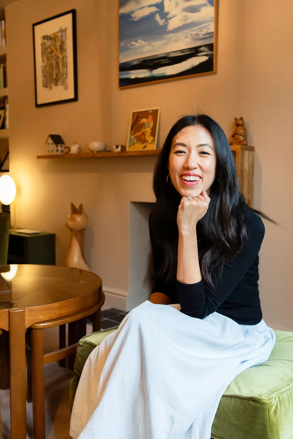 Jennifer Chong smiling while leaning on her hand, wearing a white top and white trousers, seated indoors