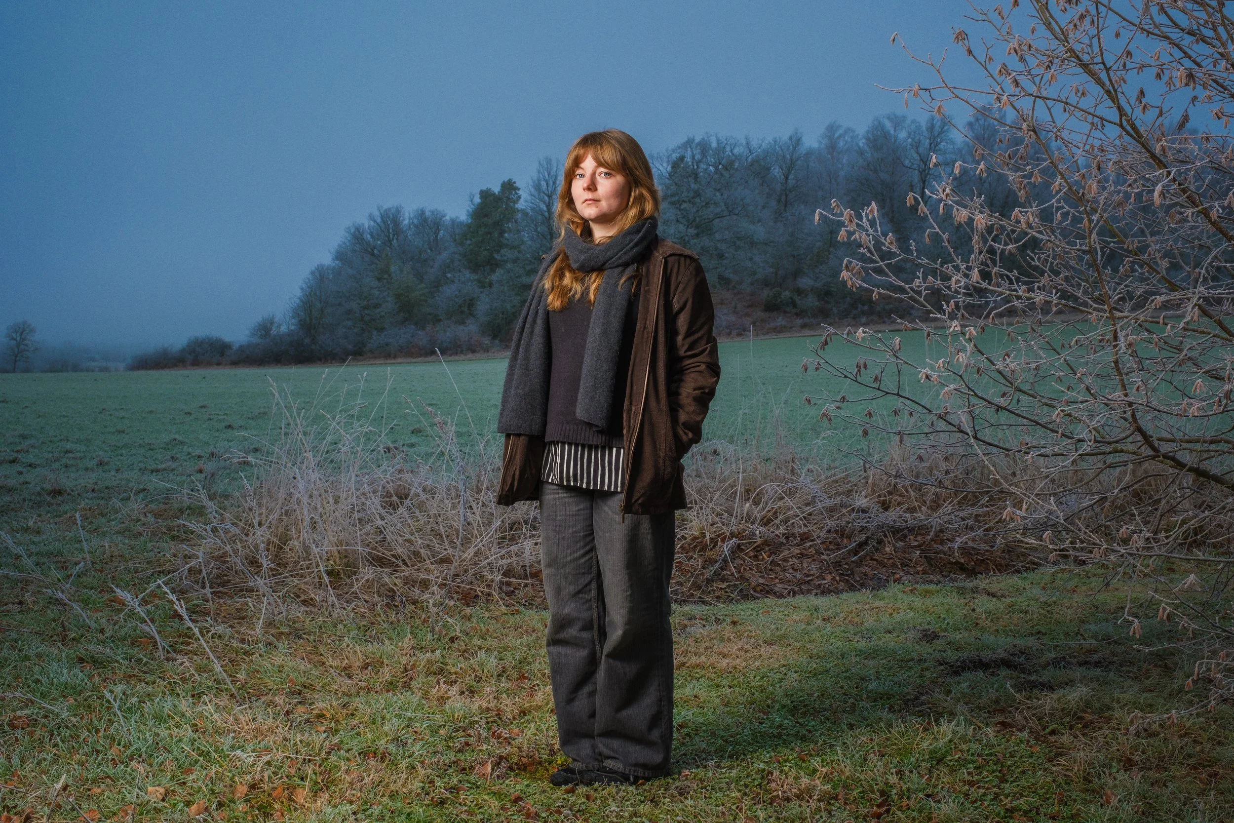 En kvinna står i ett grönt fält med träd och en blå himmel i bakgrunden.