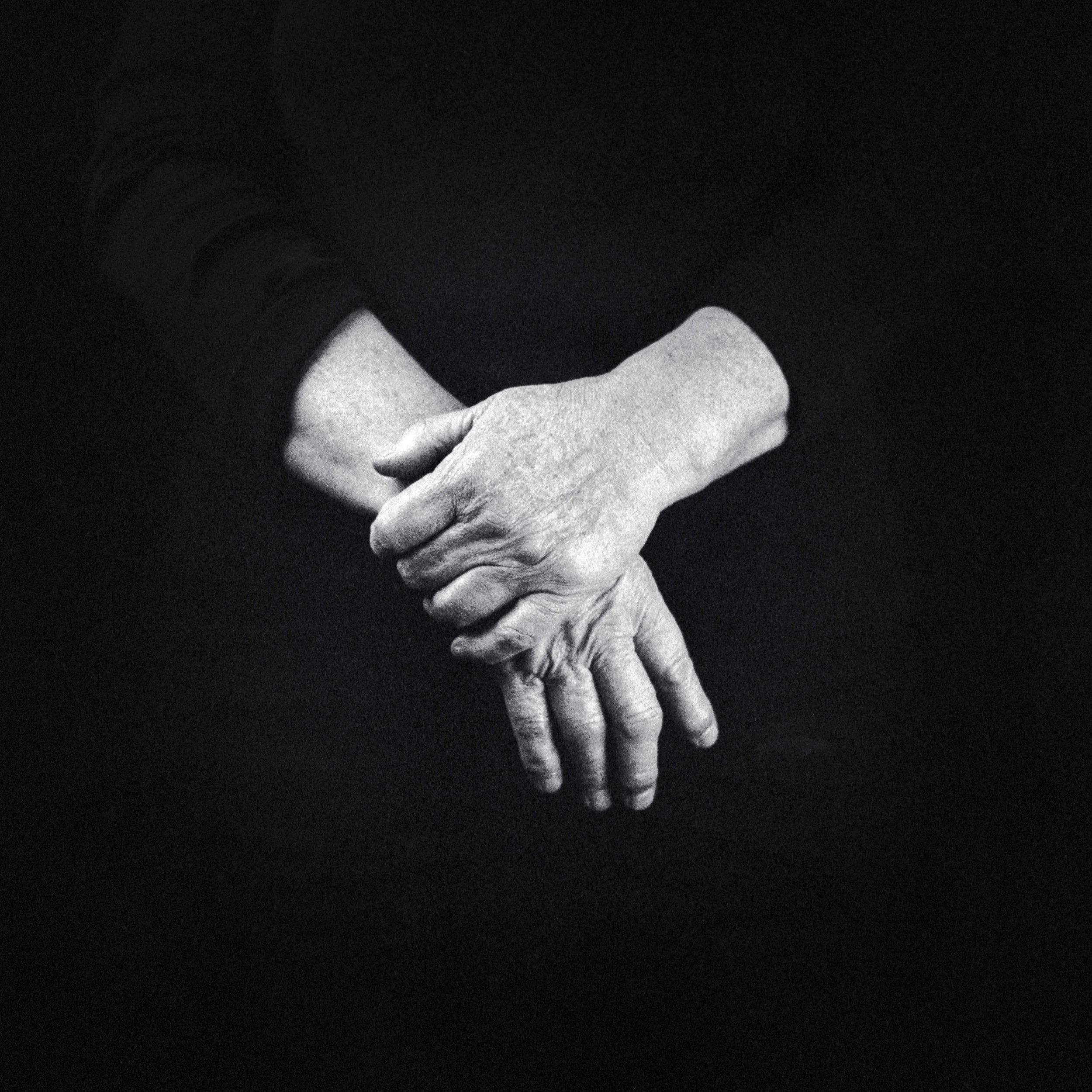 Två händer, en äldre persons och en yngre persons, som håller varandra mot en svart bakgrund.