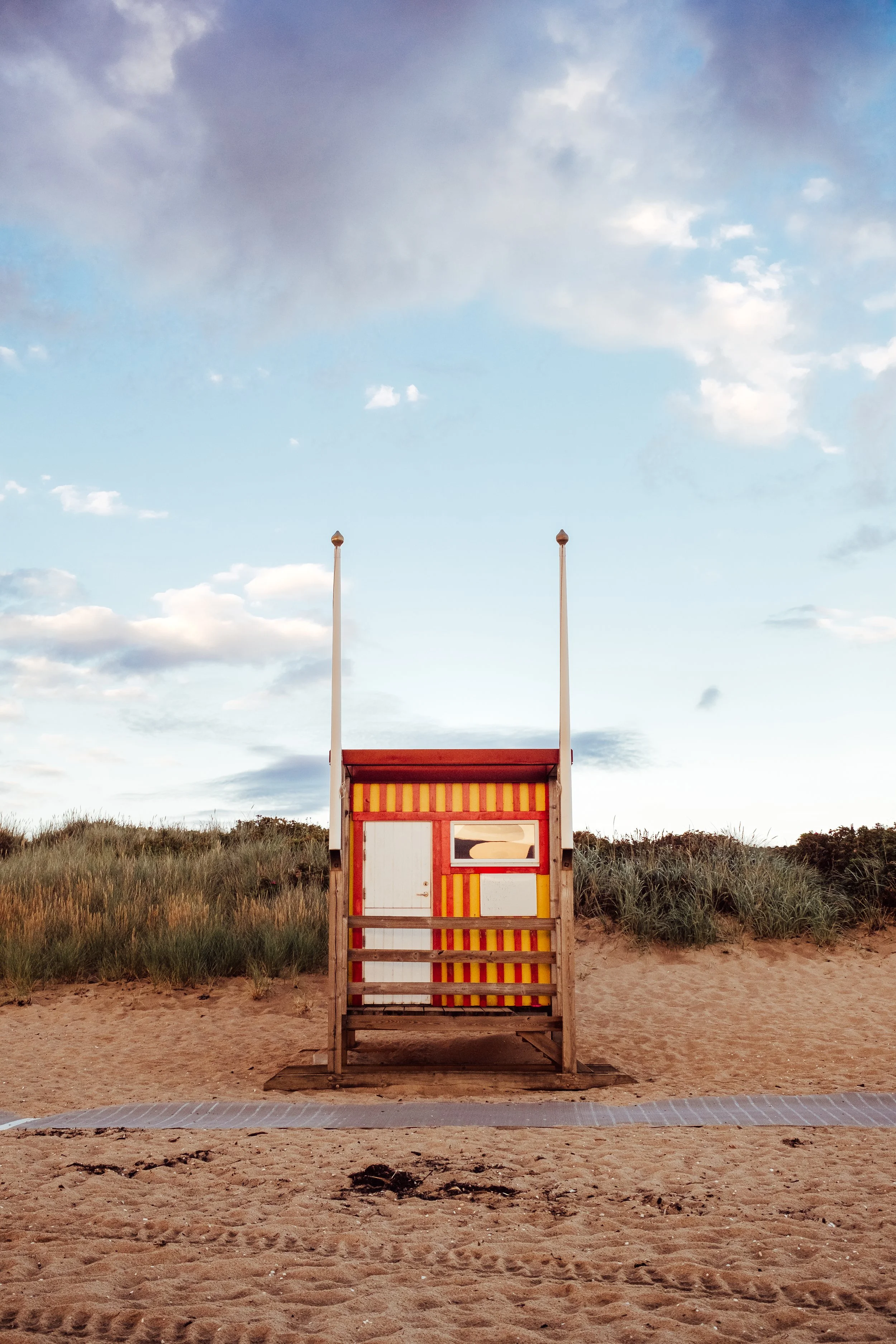 En liten fyrbyggnad på stranden med blå himmel och några moln i bakgrunden.