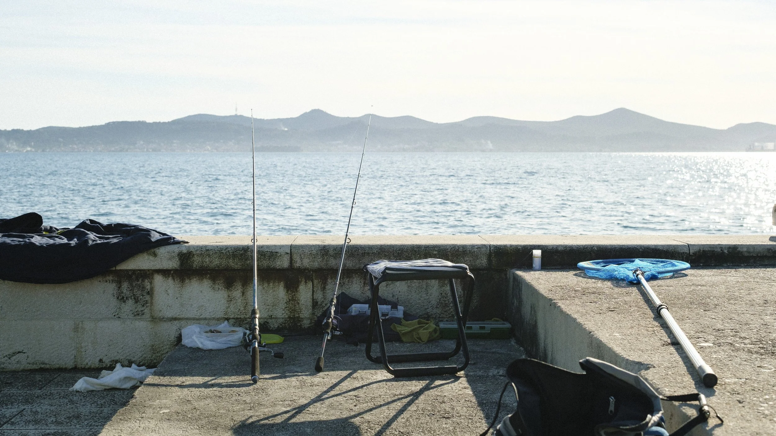 Fiskeredskap och utrustning står på en hamnkant vid havet med fjärran öar i bakgrunden.