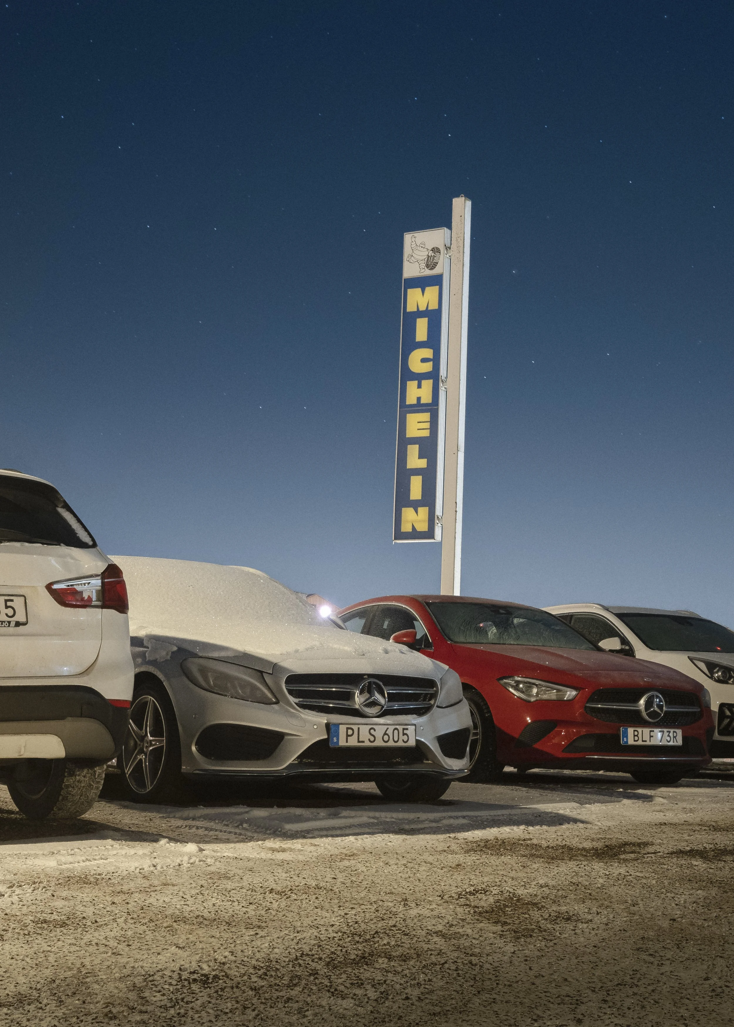 Flera bilar parkerade framför en tallrikskylt med texten 'Michelin' mot en nattig himmel.