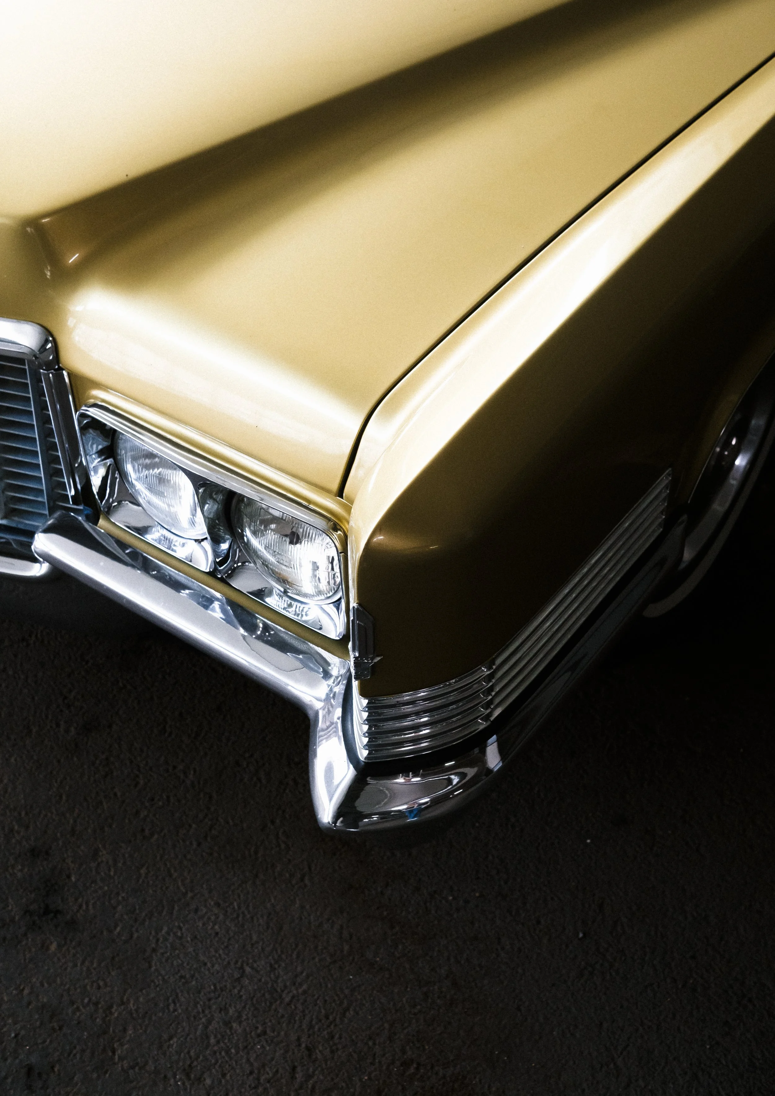 En gul vintage bil med kromdetaljer, visad från fronten, med fyrhjuliga lampor och en del av frontgrillen.