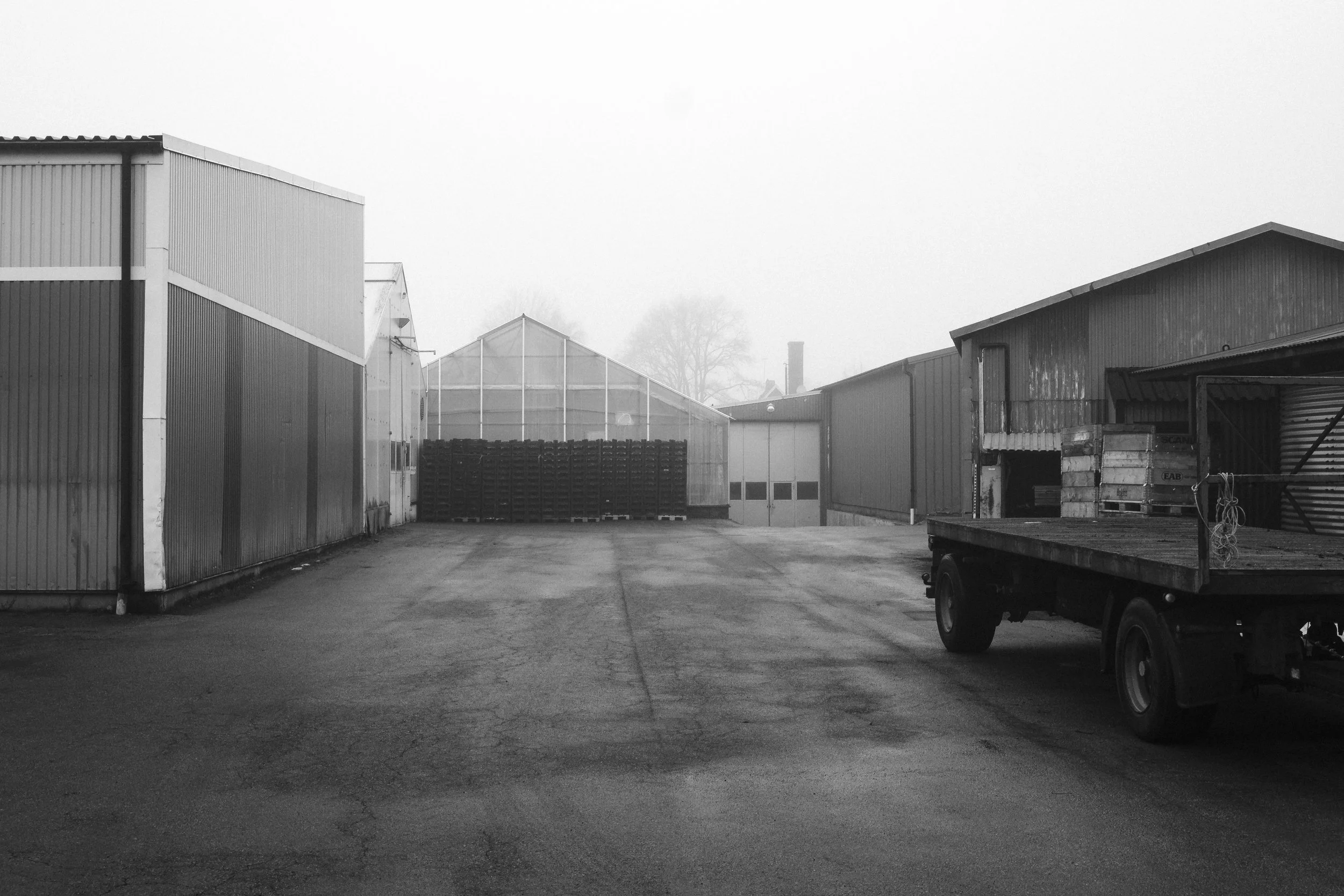 En svartvit bild av en inhägnad industriområde med berg- och dalbågar och ett tomt lastbilssläp till höger.