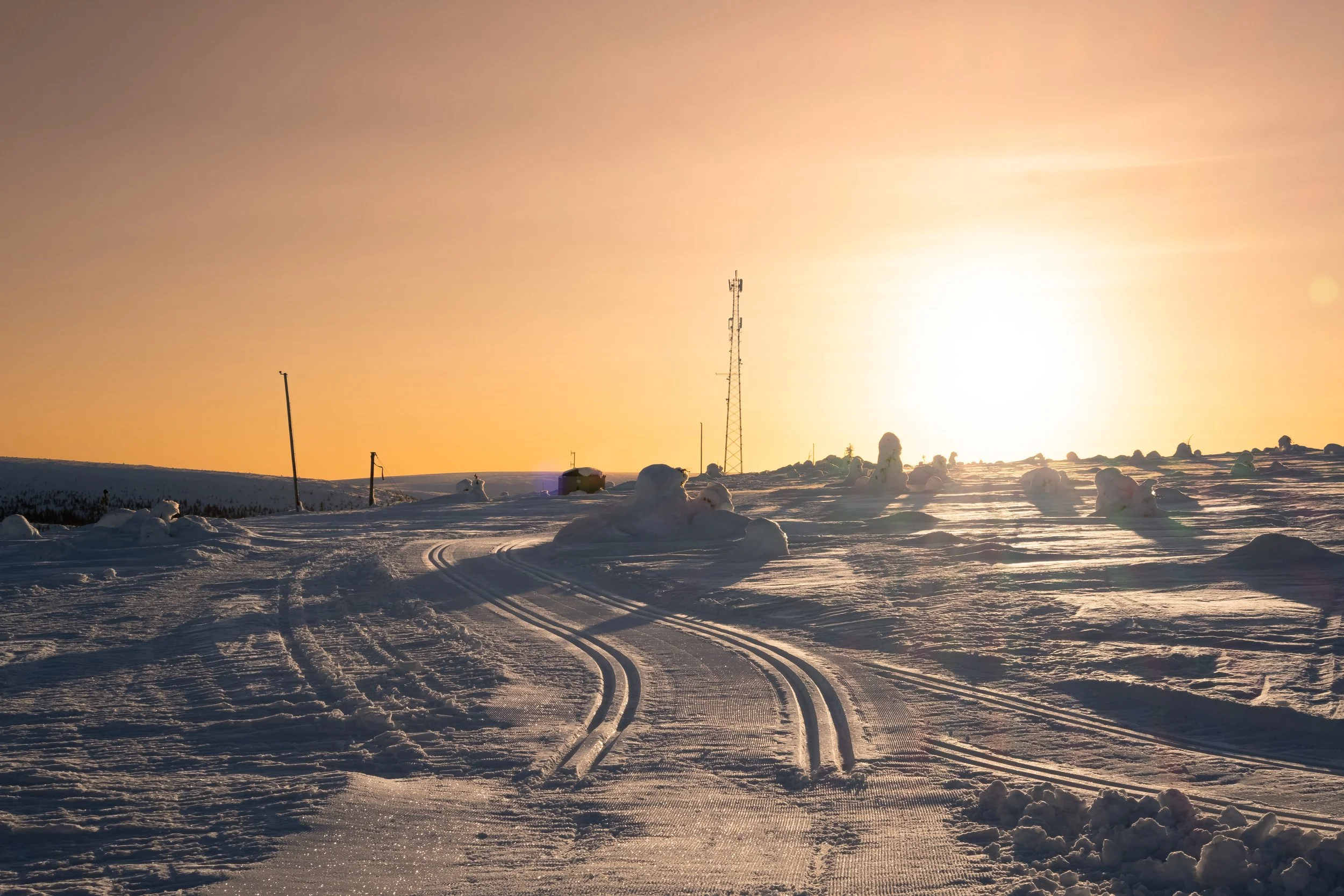 Snötäckta landskap med skidspår och snögubbar under solnedgång i Sverige.