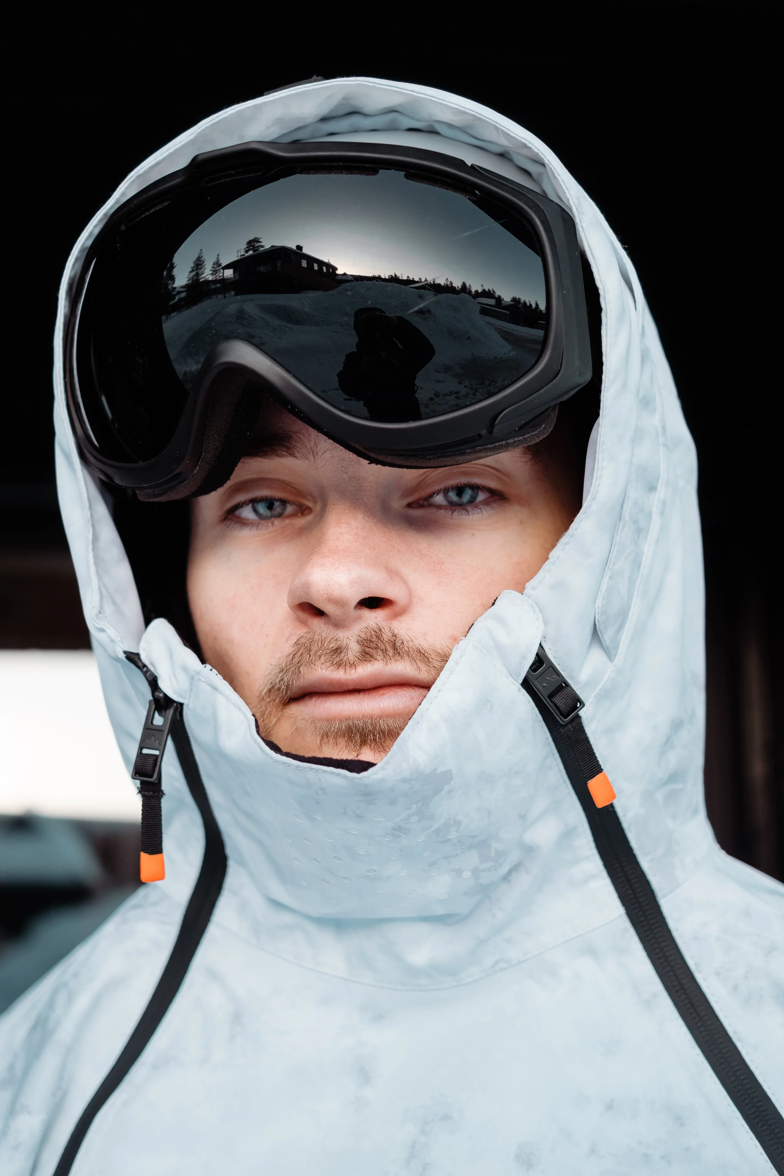 Man i vit skidjacka med skidglasögon på huvudet, reflekterande glas visar snölandskap och byggnad