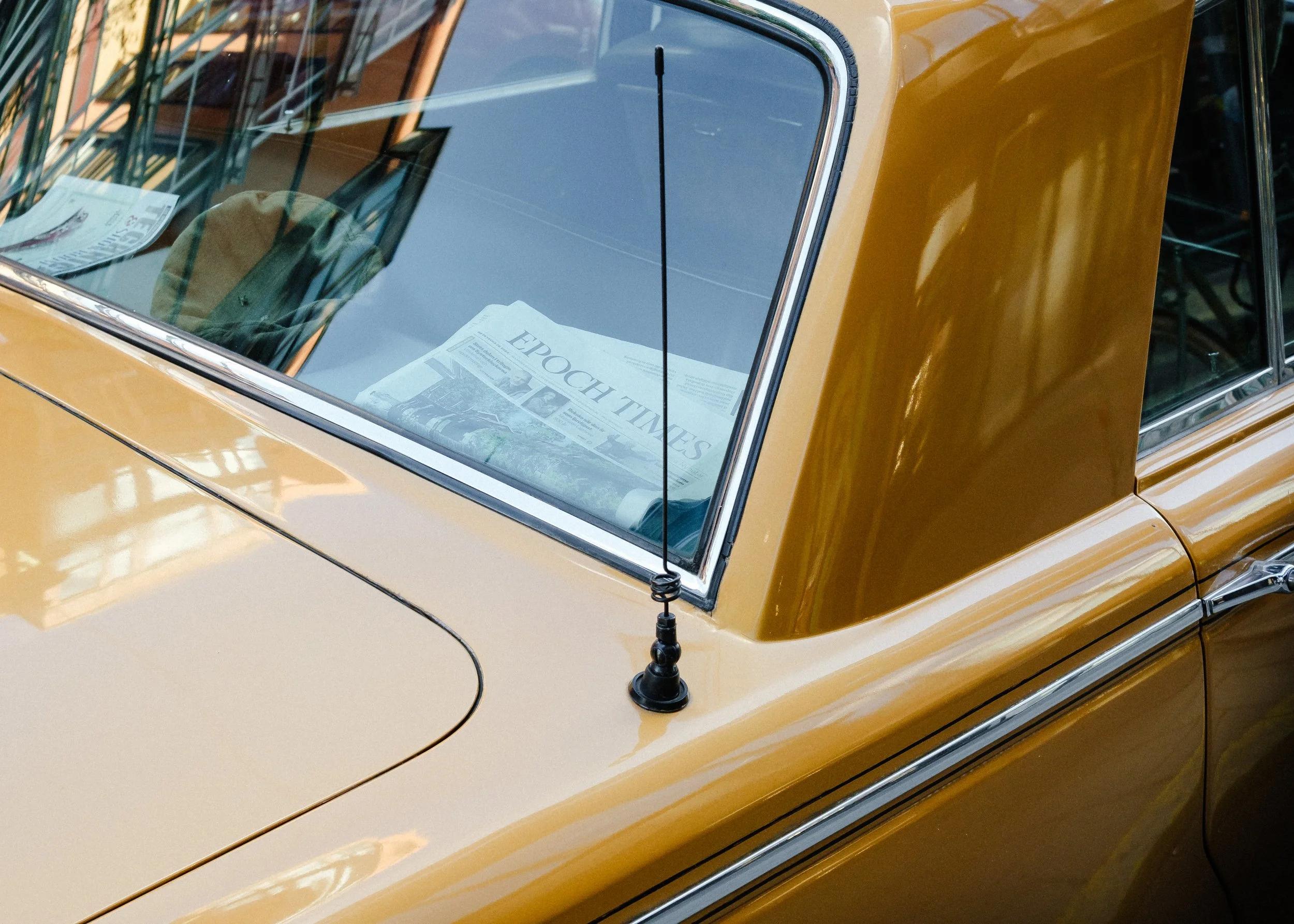 Närbild av en gul bils vindruta med ett tidningsblad bakom glaset, och en svart radiosändareantenn på taket.