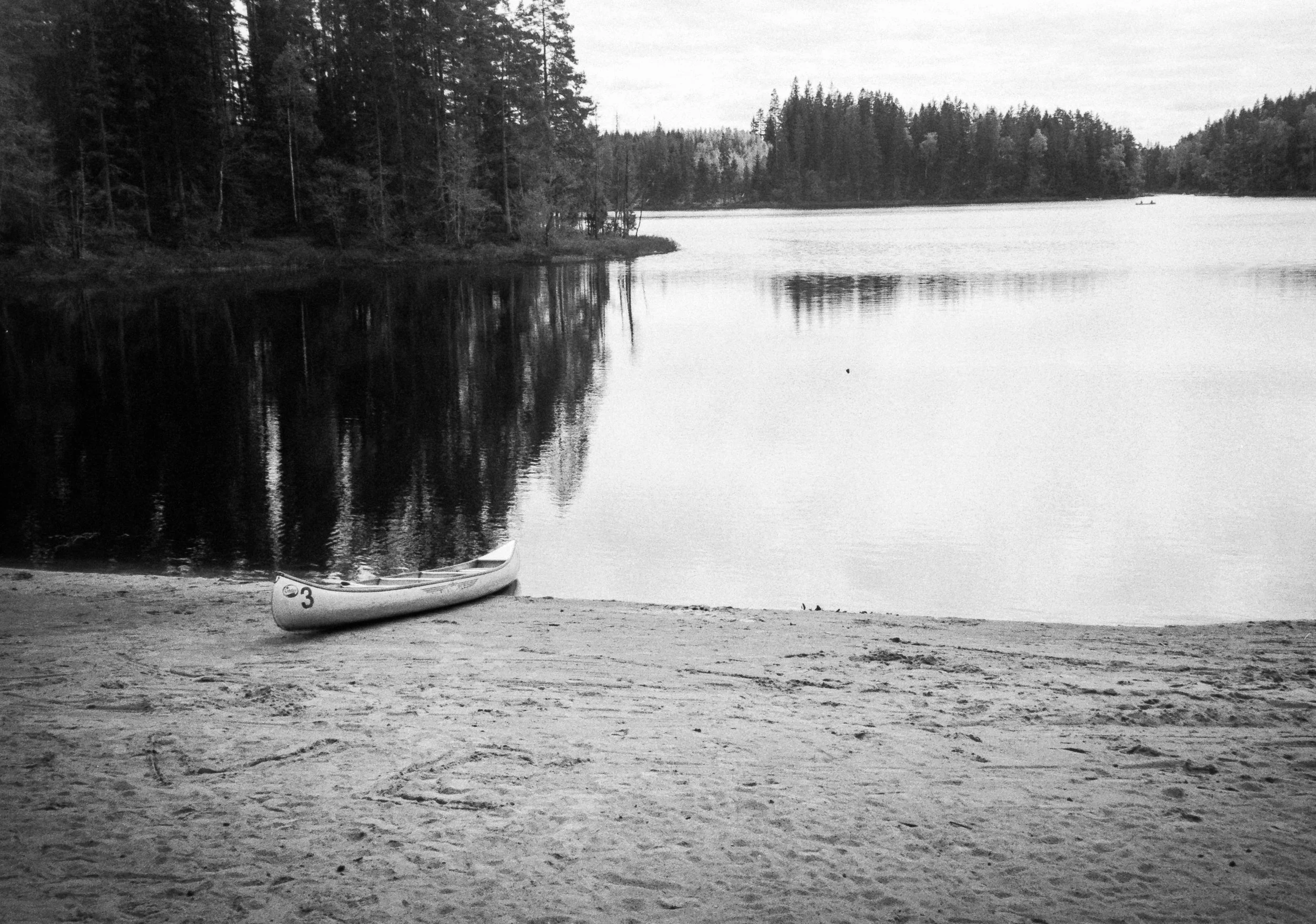 En u-båt ligger på en sandstrand vid en sjö, omgiven av träd på båda sidor av vattnet.