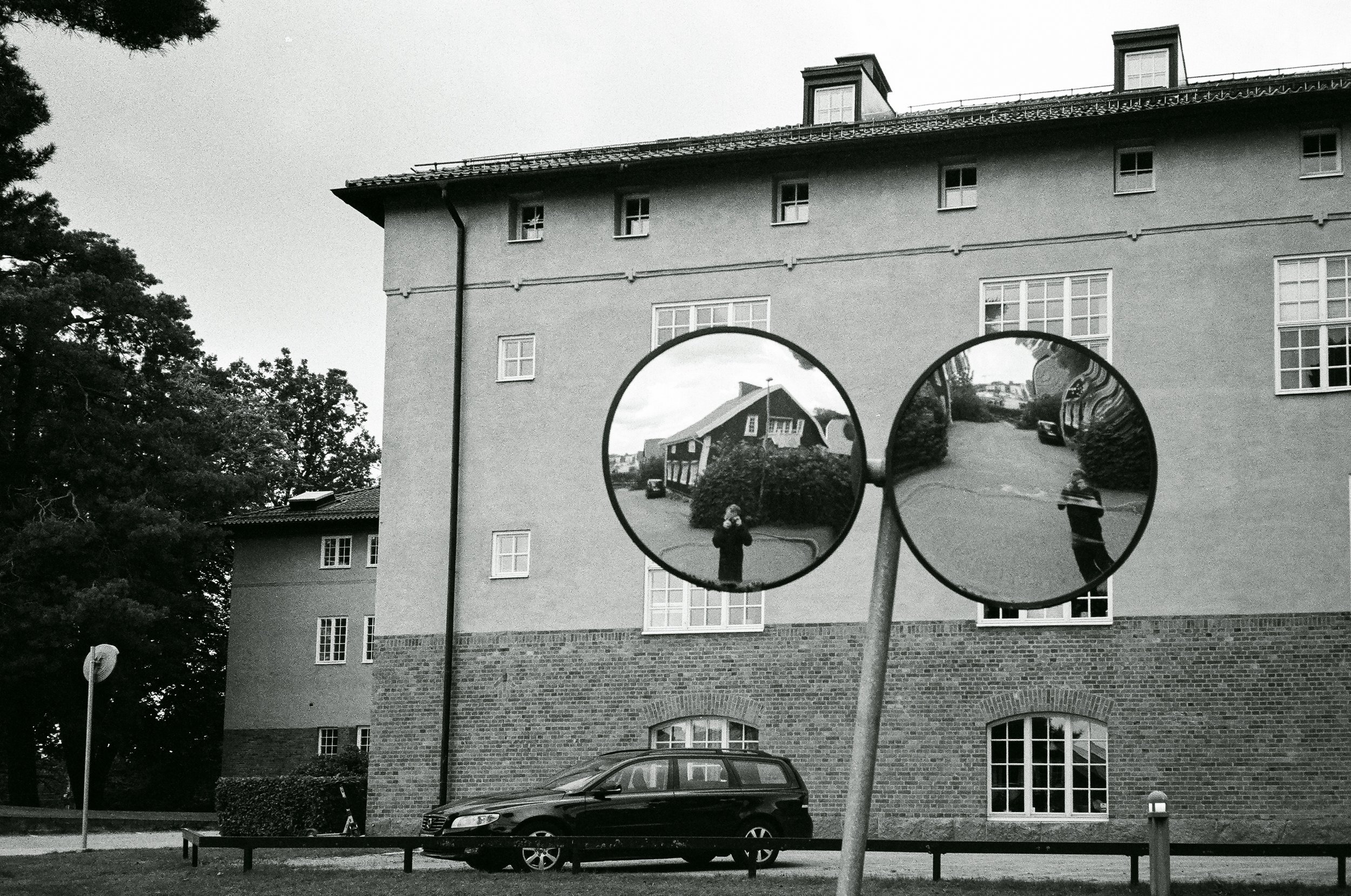 Två runda trafikreflexer reflekterar en person som tar ett foto och ett hus i omgivningen.
