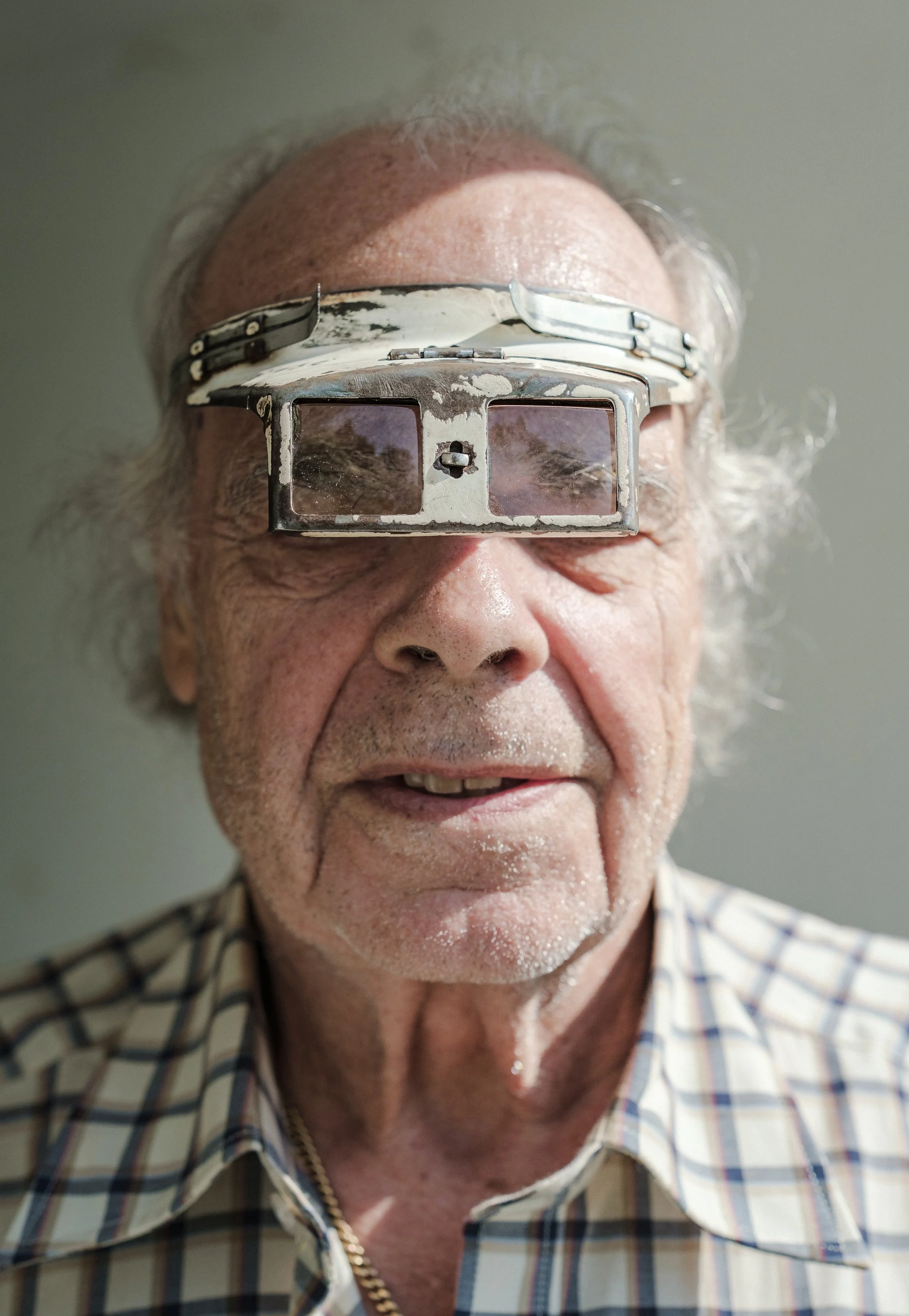 Äldre man med glasögon som har ett reflektionsglas, klädd i rutigt skjorta.