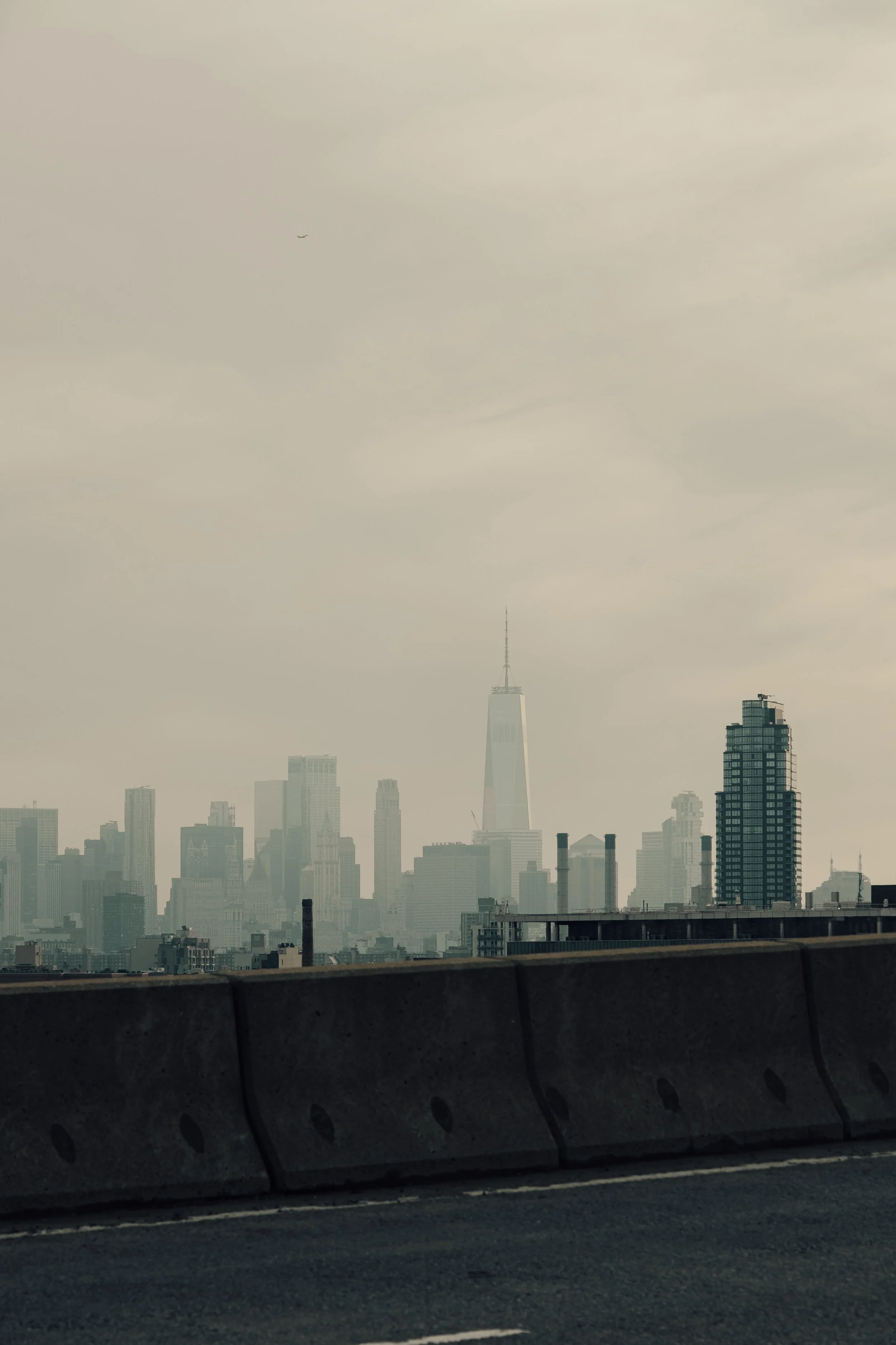 Vy över Manhattan med skyskrapor, inklusive One World Trade Center, i grumlig himmel.