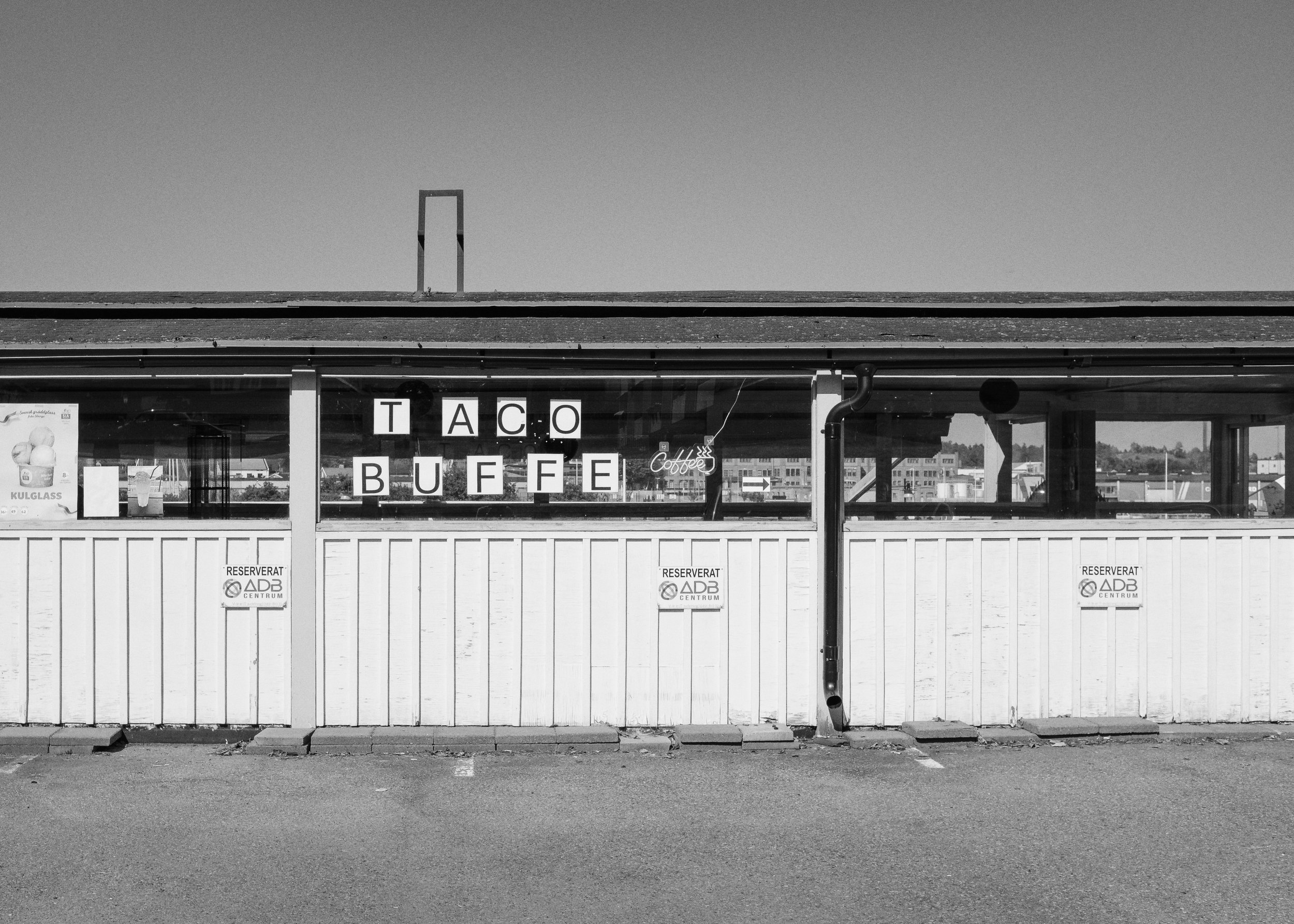 Svartvitt bild av en restaurang med skylten 'Taco Buffet' på fönstret.