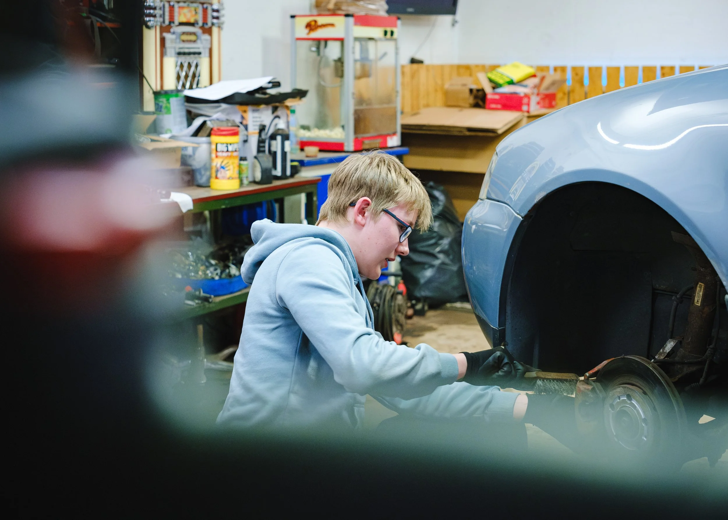 En person arbetar på ett bildäck i en verkstad, med bilen lyft för att kunna arbeta på hjul och broms.