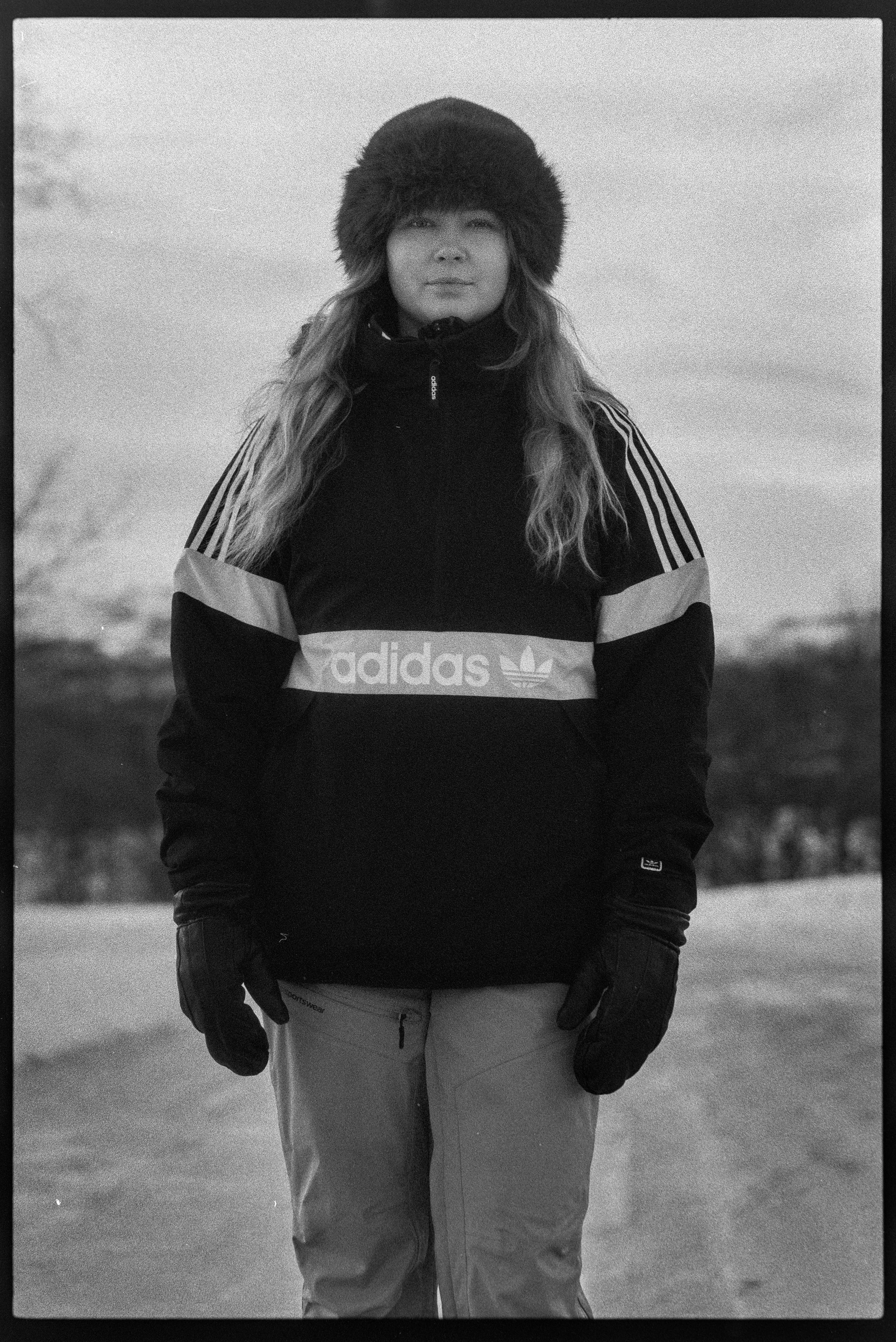 En kvinna i vinterkläder, inklusive huva, stående utomhus i snölandskap, svartvitt fotografi.