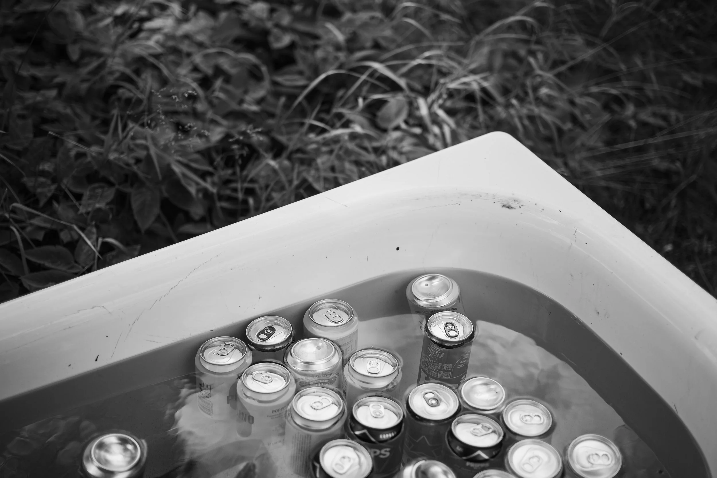 En badtunna fylld med vatten och burkar flytande på ytan, utomhus med gräs och växter runt.