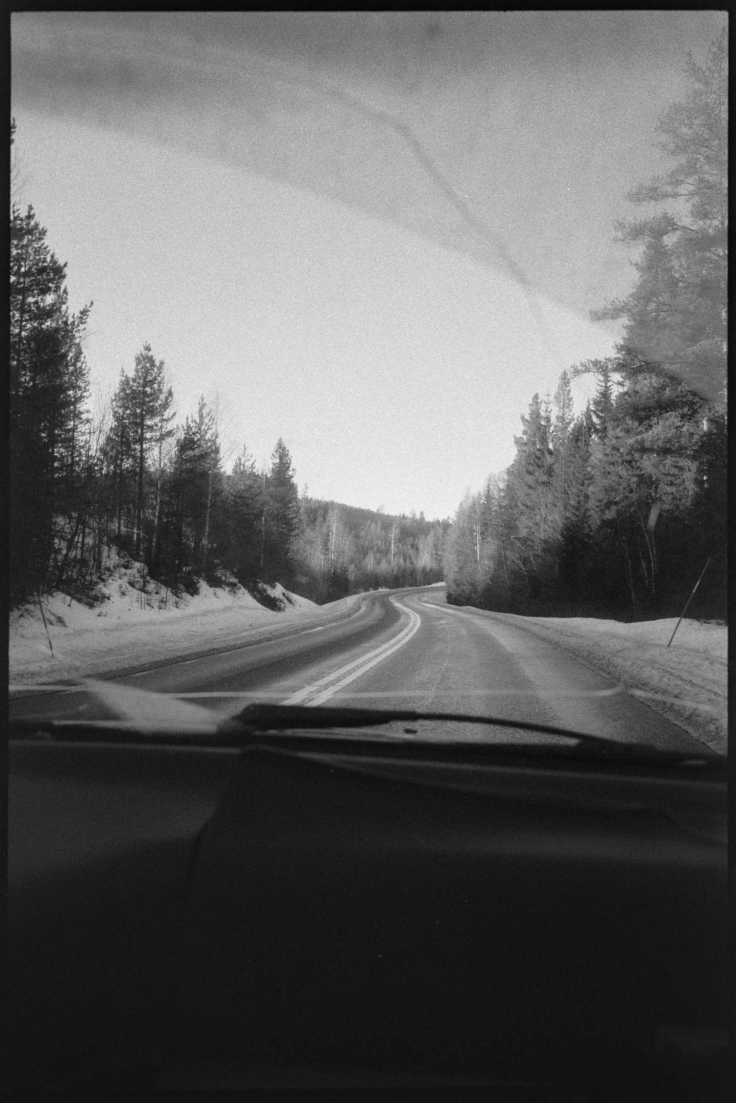 En svartvit bild av en väg som slingrar sig genom ett skogsområde med träd på båda sidor.