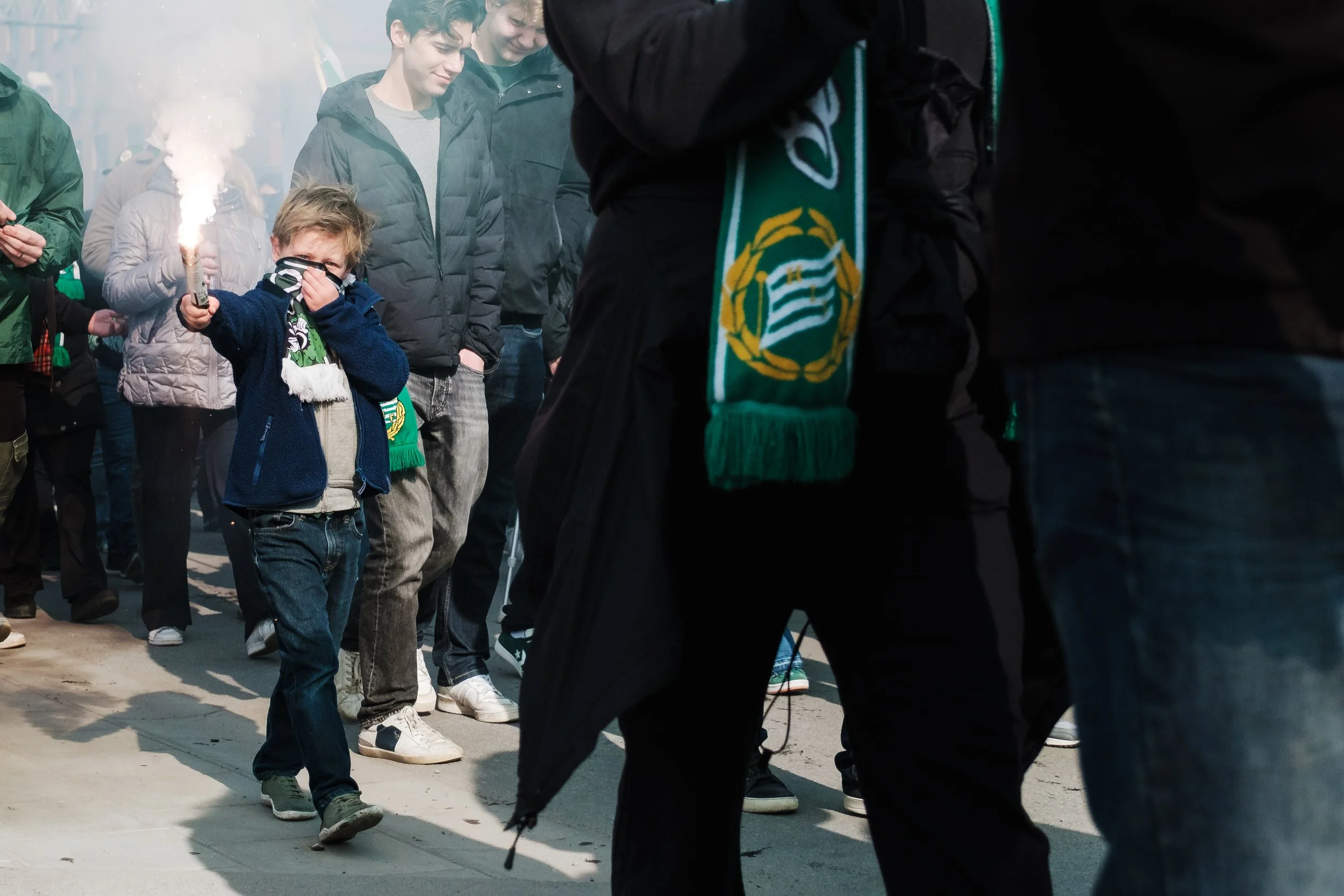 Ung man som håller ett fackla och skymtar i en folksamling, många är klädda i varma jack och mössor.