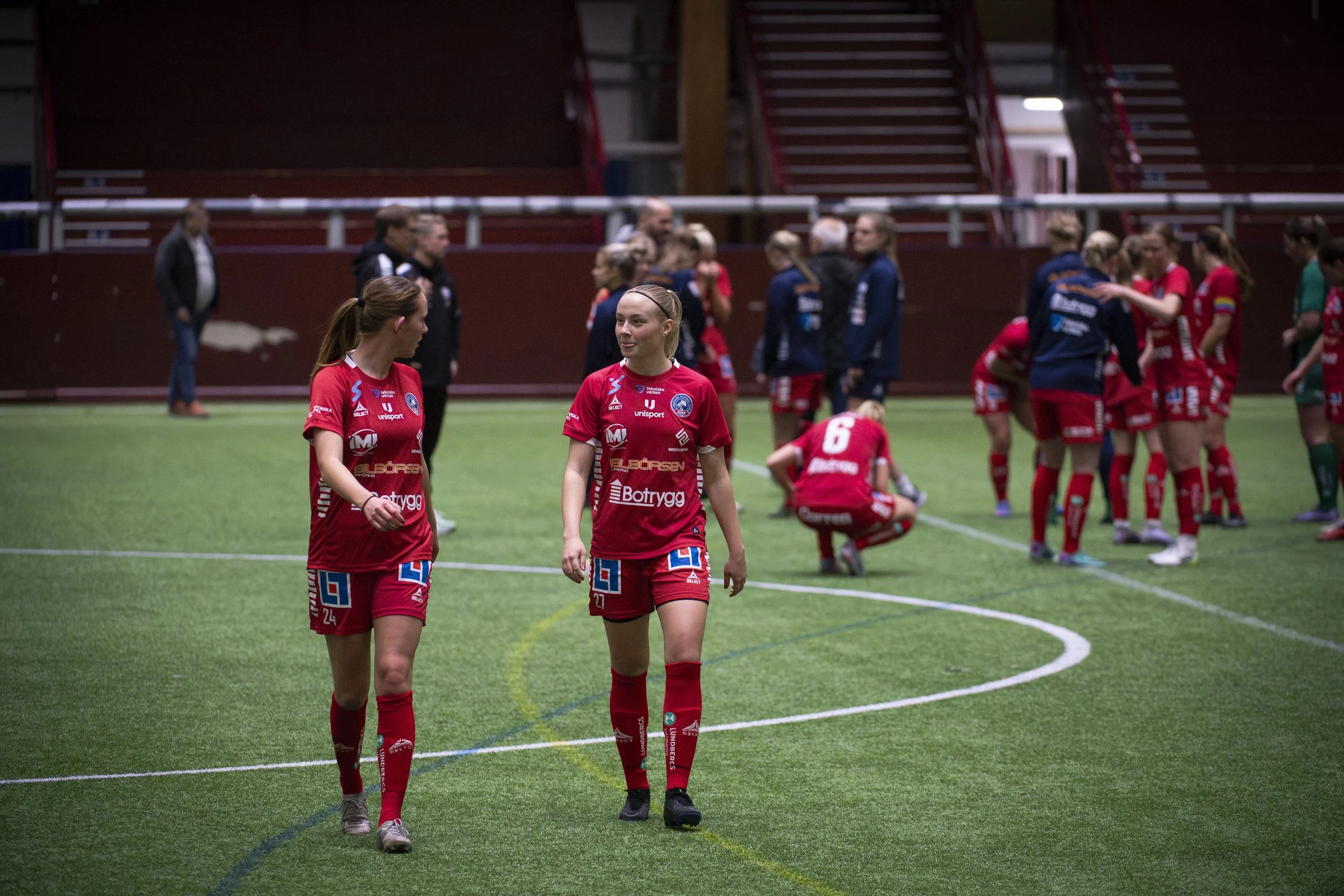 Fotbollsspelare i rött dräkter på en inomhusfotbollsplan efter matchen, några samtalar och andra samlas i grupper.