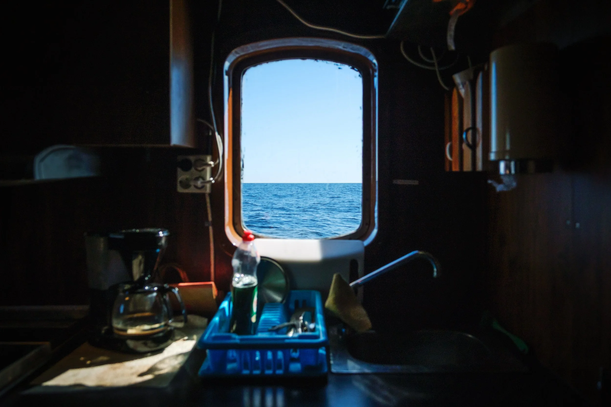 Interiör av ett kök ombord på en båt, med ett fönster som visar havet utanför.