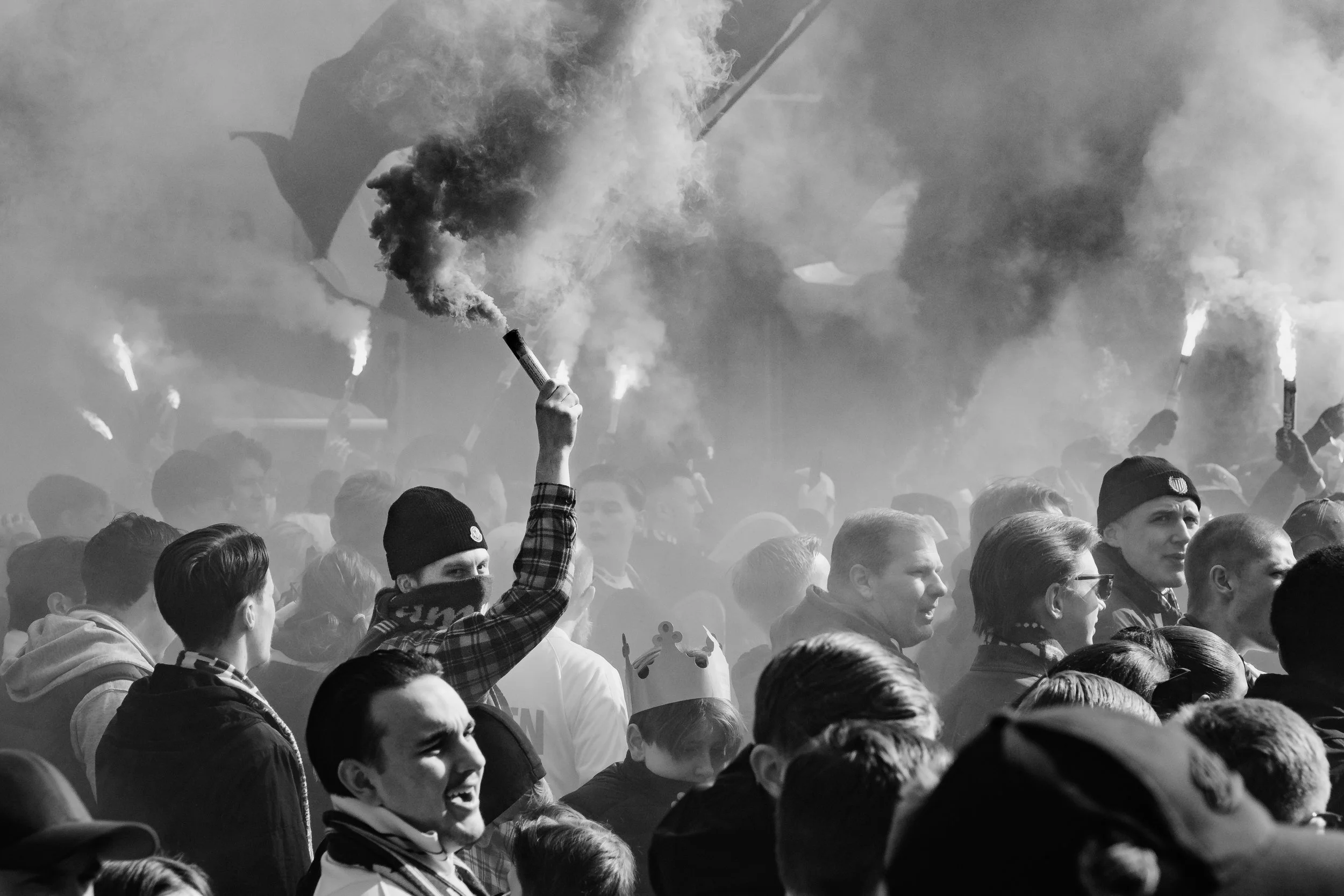 En stor folkmassa av människor som håller facklor, en person håller upp en fackla i mitten av bilden. Människorna är klädda i vardagskläder, några bär mössor och ett barn har krona. Svartvitt bild.