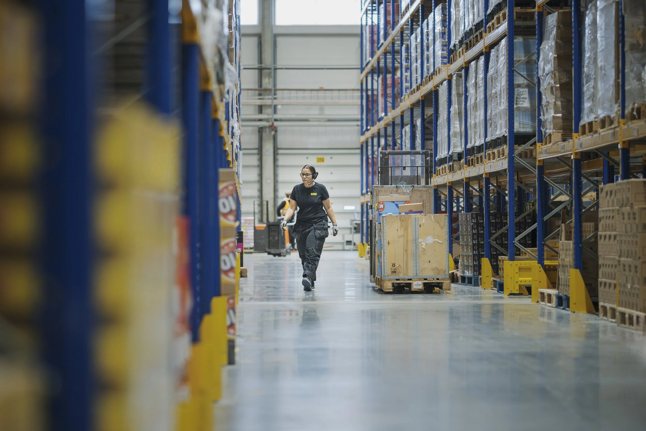 En person i en lagerhall går längs med hyllor fyllda med varor.