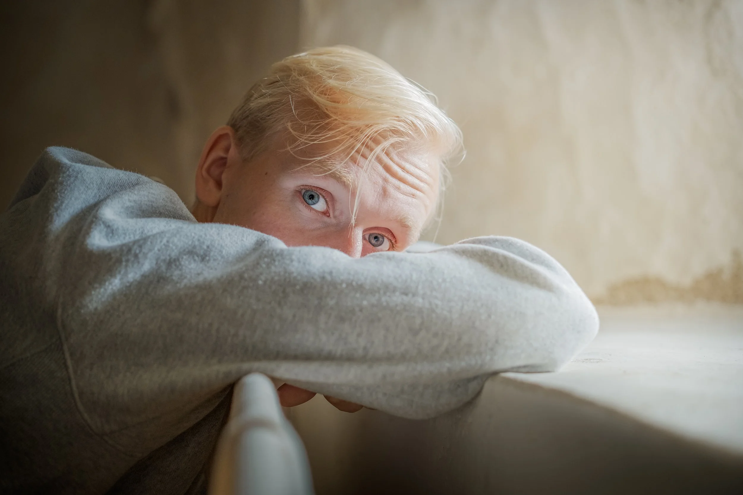 Ung man med blont hår som vilar sitt huvud på armbågen och tittar ut genom ett fönster.