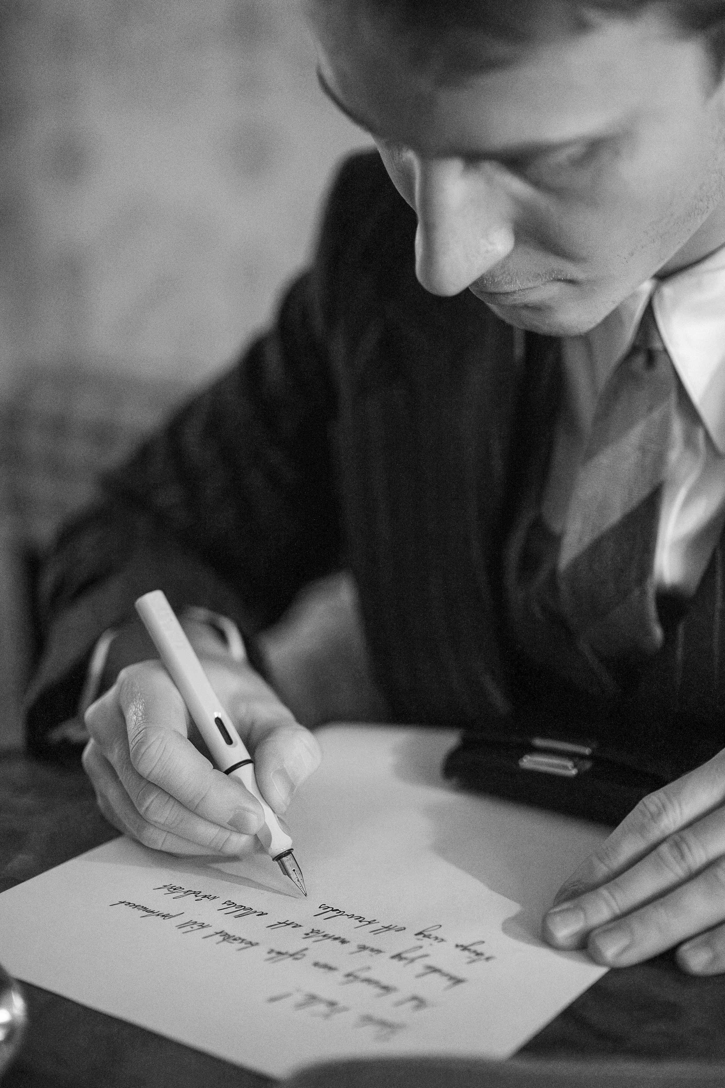 En person skriver ett handskrivet meddelande på ett papper med en vit penna, svartvitt foto.