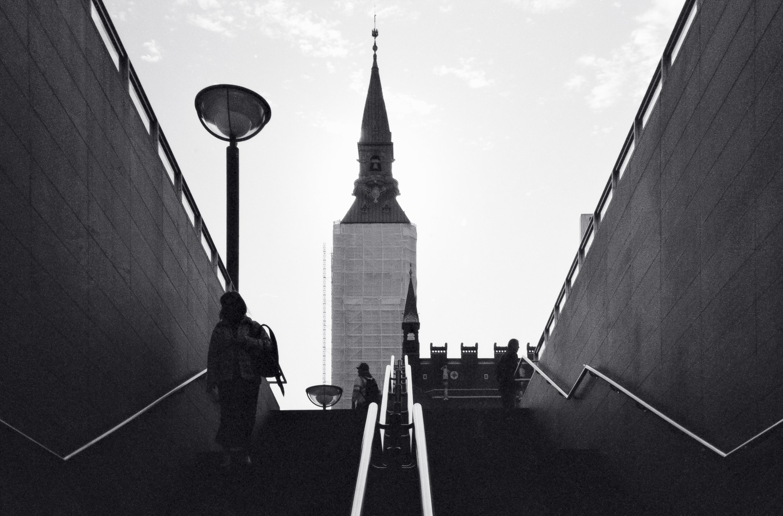 Personer som går uppför en trappa mot en kyrktorn i bakgrunden i en svartvit bild.